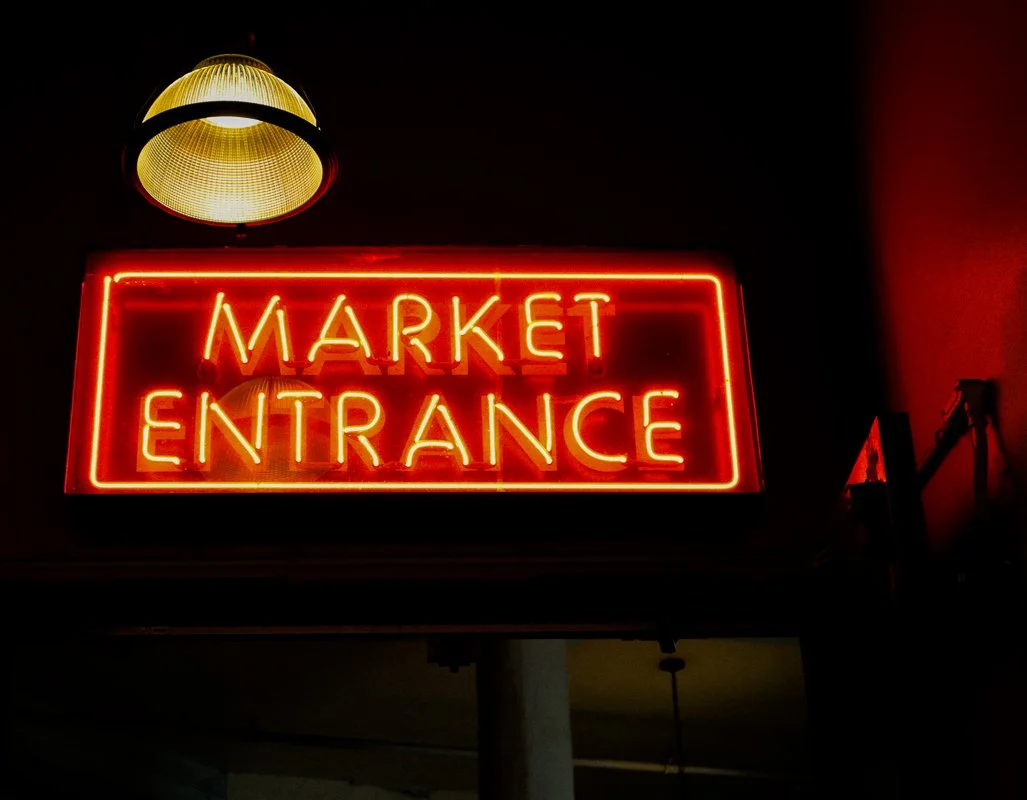 Neon sign reading 'Market Entrance' with a hanging light above.