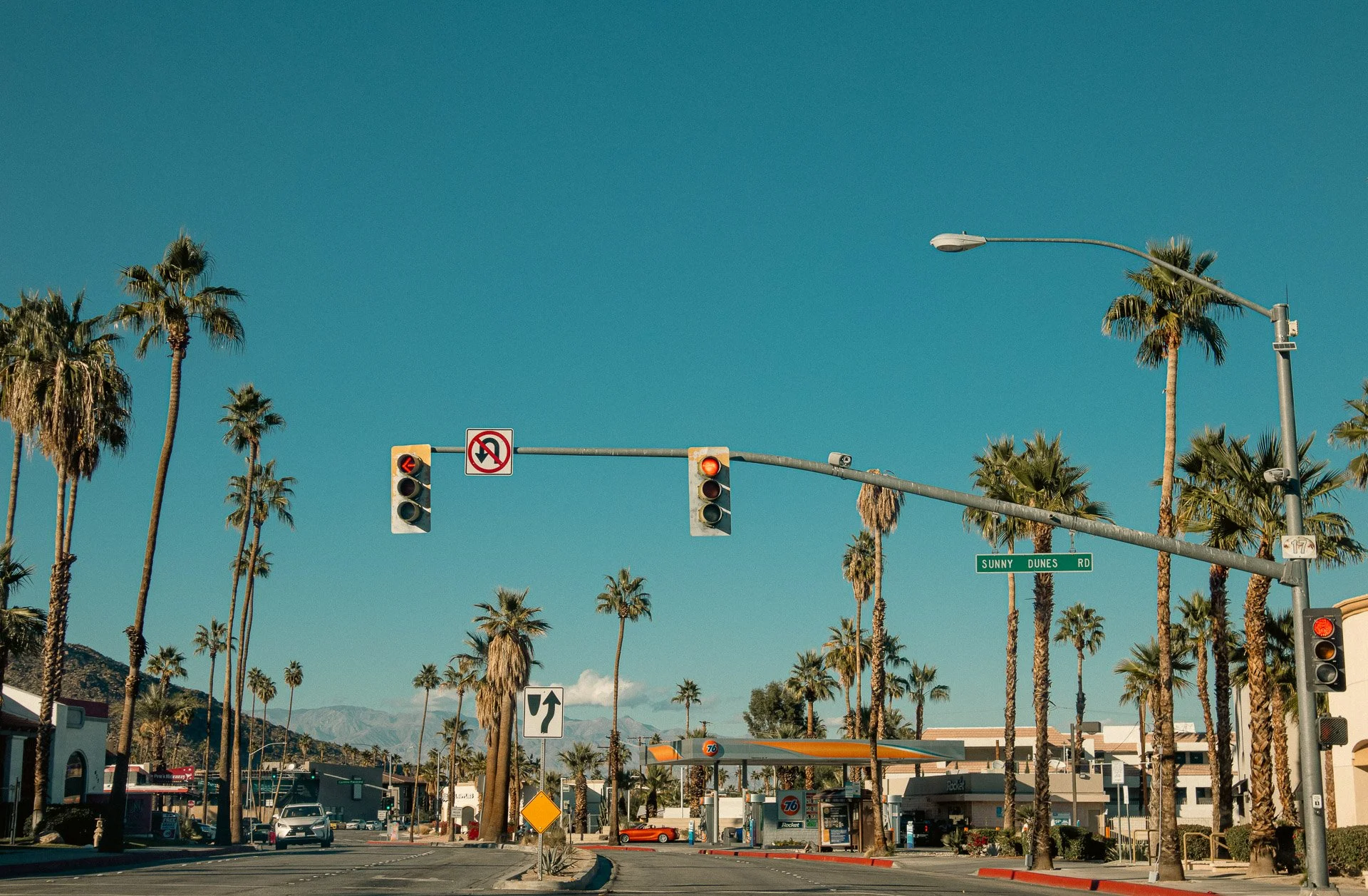 Palm tree-lined street intersection with traffic lights, Sunny Dunes Road sign, and a gas station.