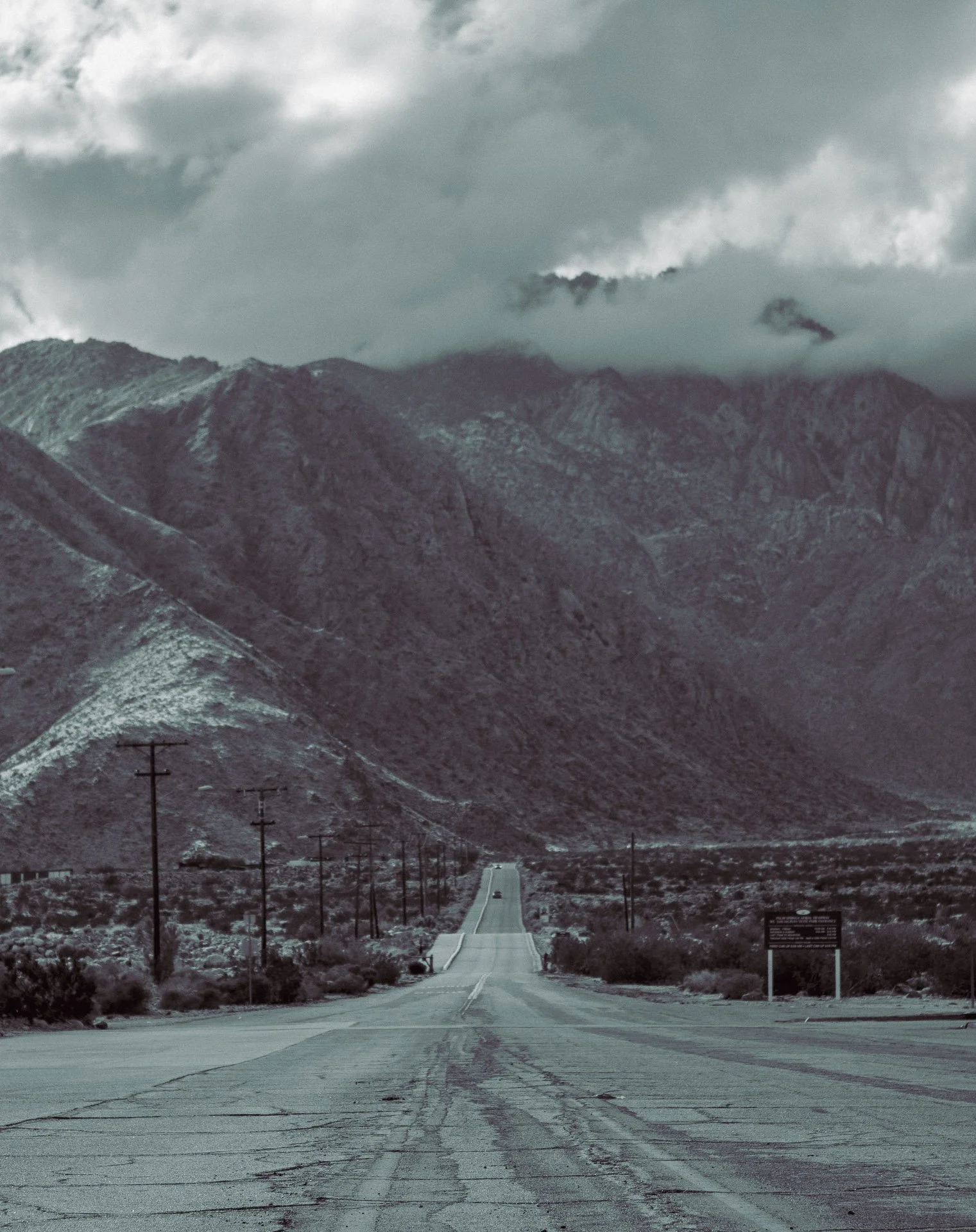 A long, empty road leading towards distant mountains under a cloudy sky.