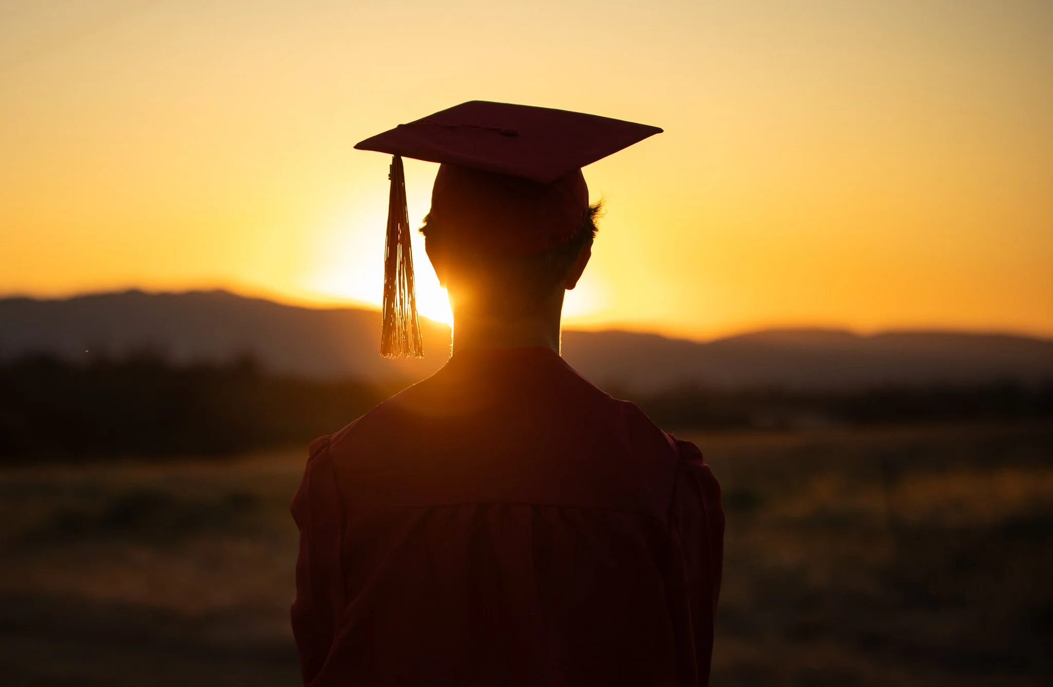 Silhouette of a graduate in cap and gown at sunset.