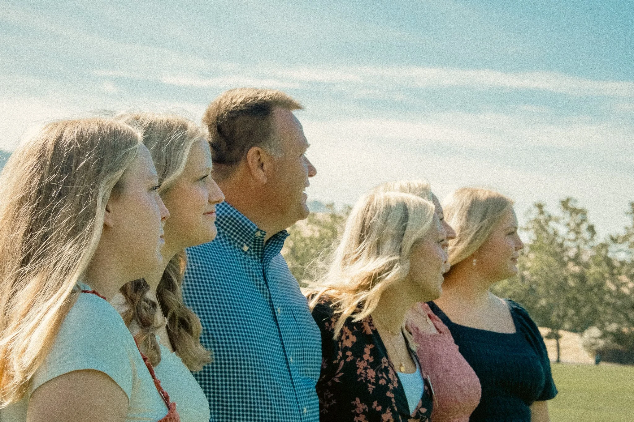 Group of people standing outdoors, smiling, with clear blue sky and trees in the background.