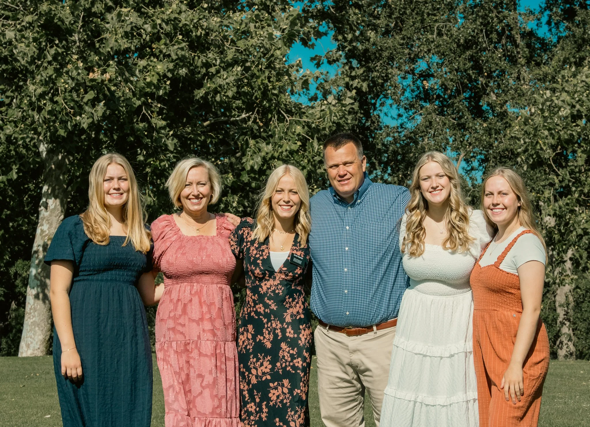 Group photo of six people standing outdoors with trees in the background.