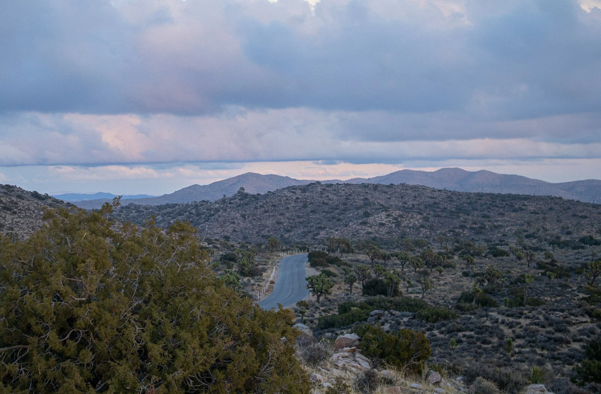 Desert landscape with a winding road, hills, and cloudy sky.