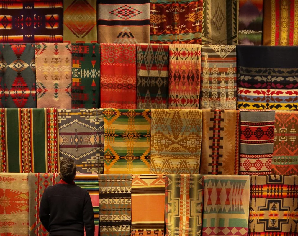 Person viewing a display of colorful, patterned textiles hanging on a wall.