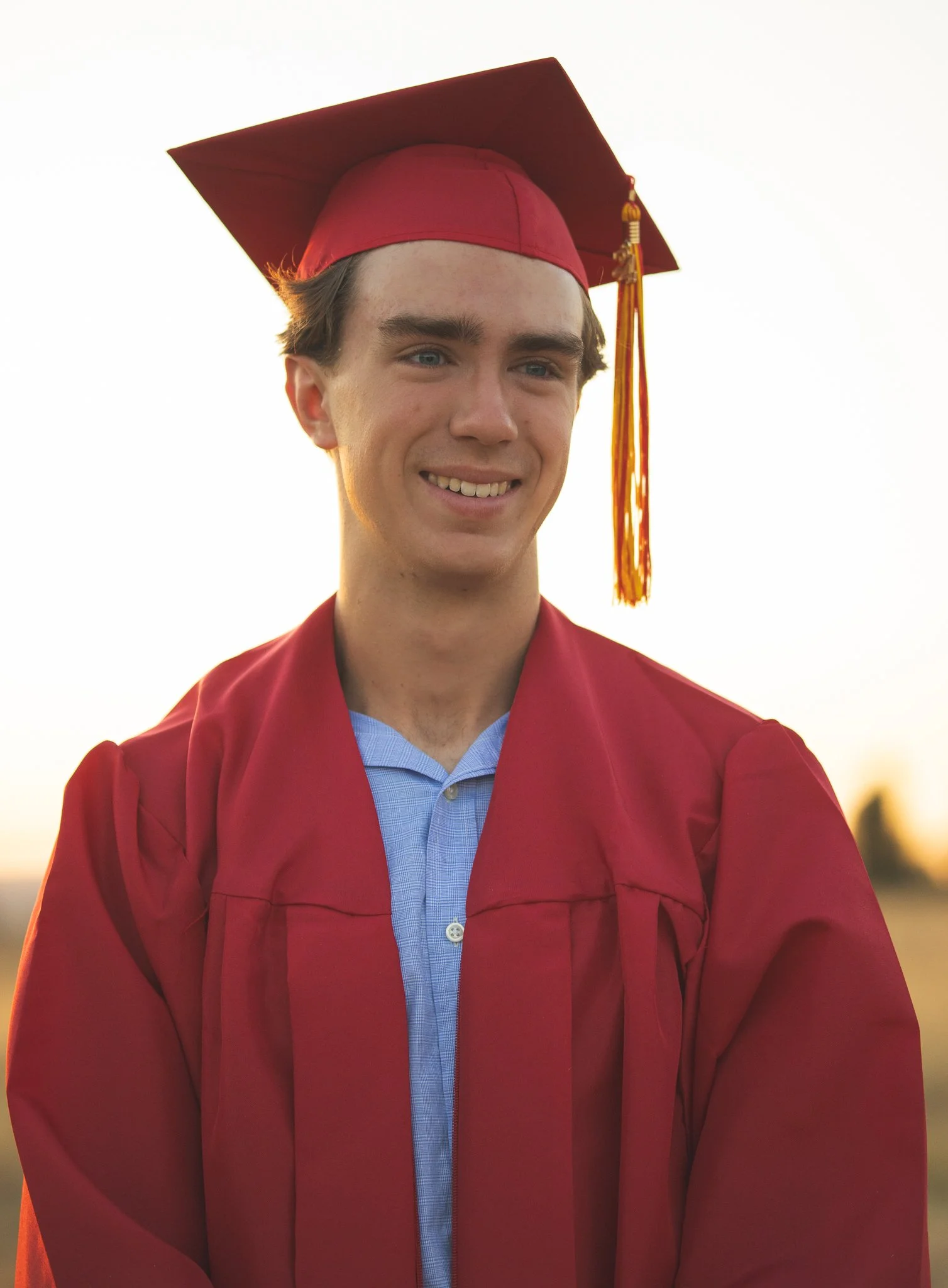 Young man wearing a red graduation cap and gown, smiling outdoors.