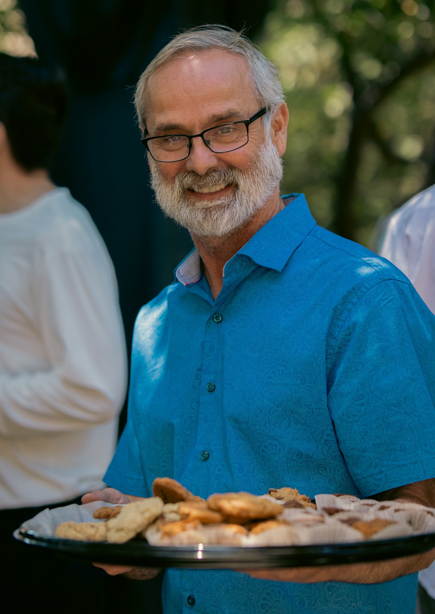 Man in glasses holding a tray of cookies outdoors.