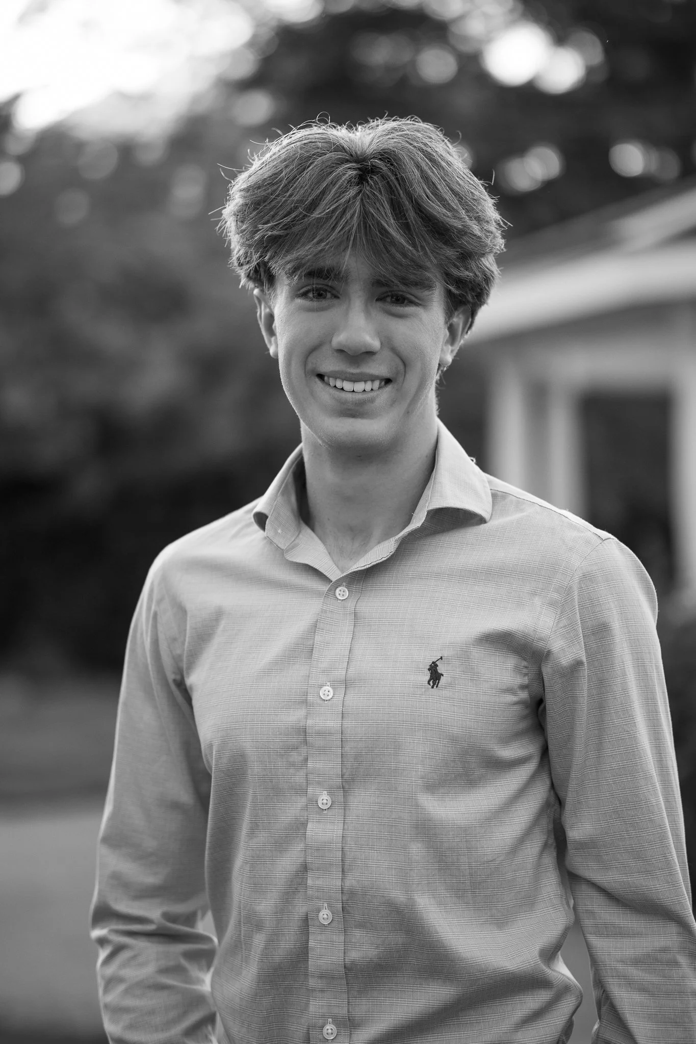 Black and white portrait of a smiling person wearing a button-up shirt outdoors.