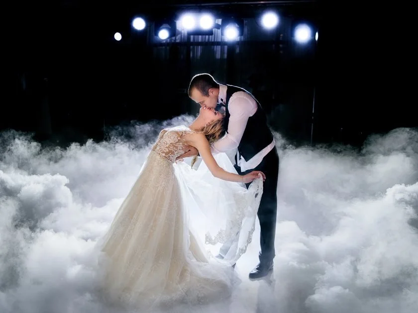 Bride and groom share a romantic dance surrounded by fog and lights at their wedding reception.