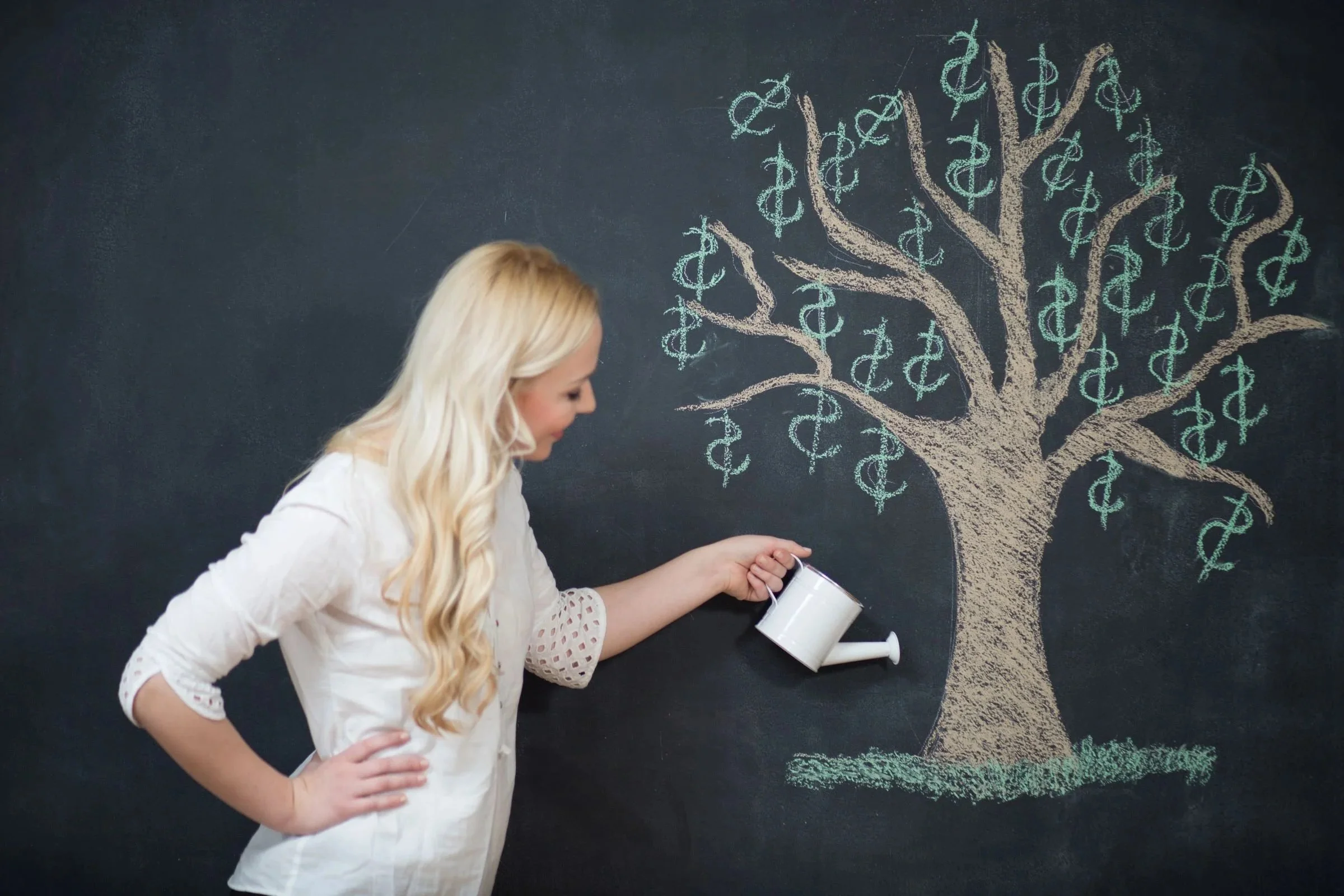 A business woman holds a watering can over a chalk-drawn money tree