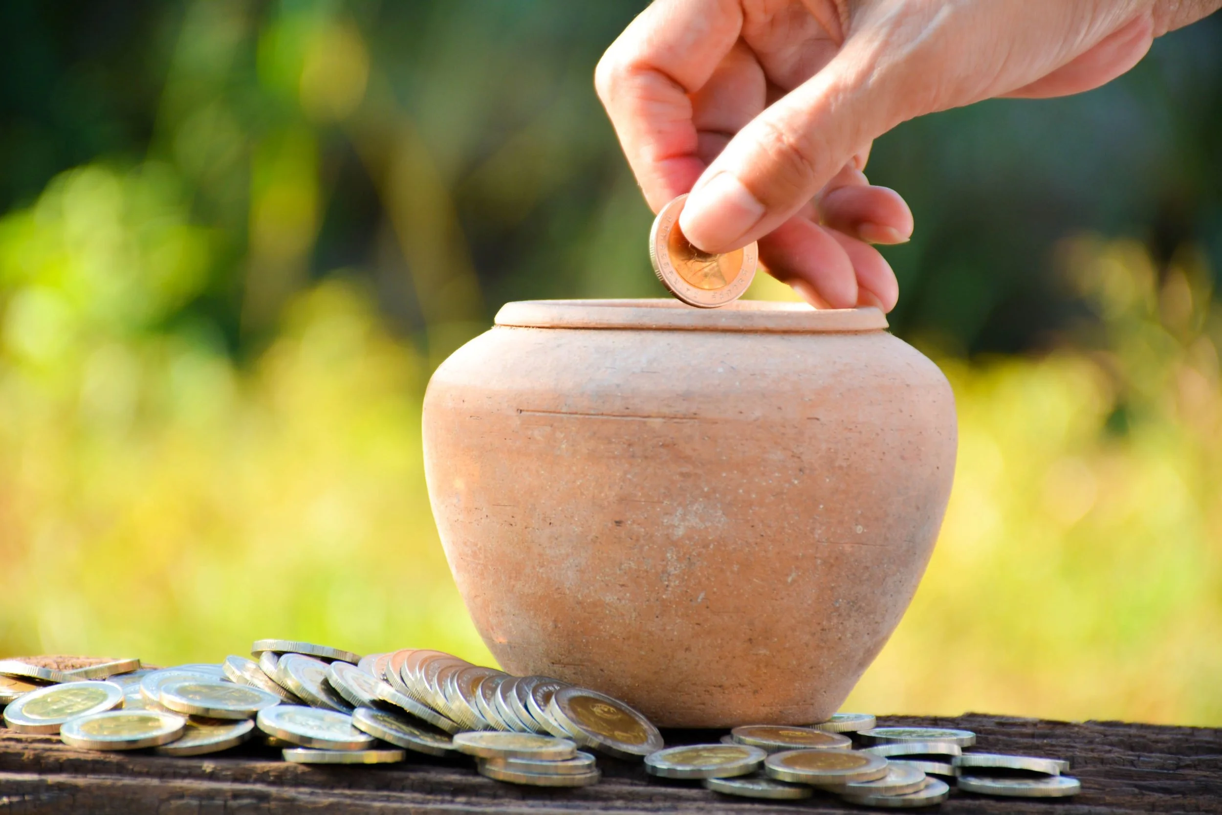 Woman dropping gold coin into clay pot with grass in background