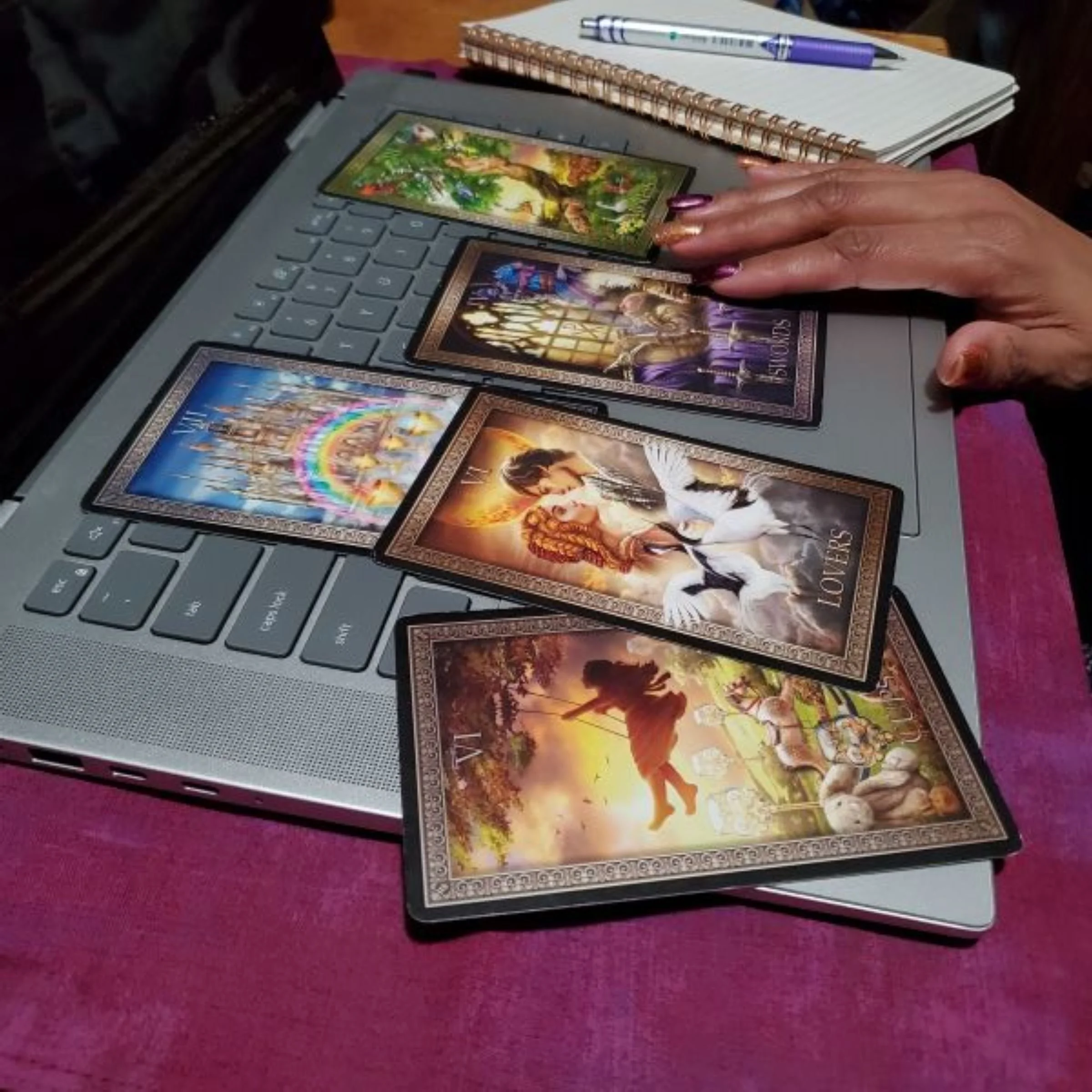 Aisha's hand with a tarot spread on her laptop next to a journal