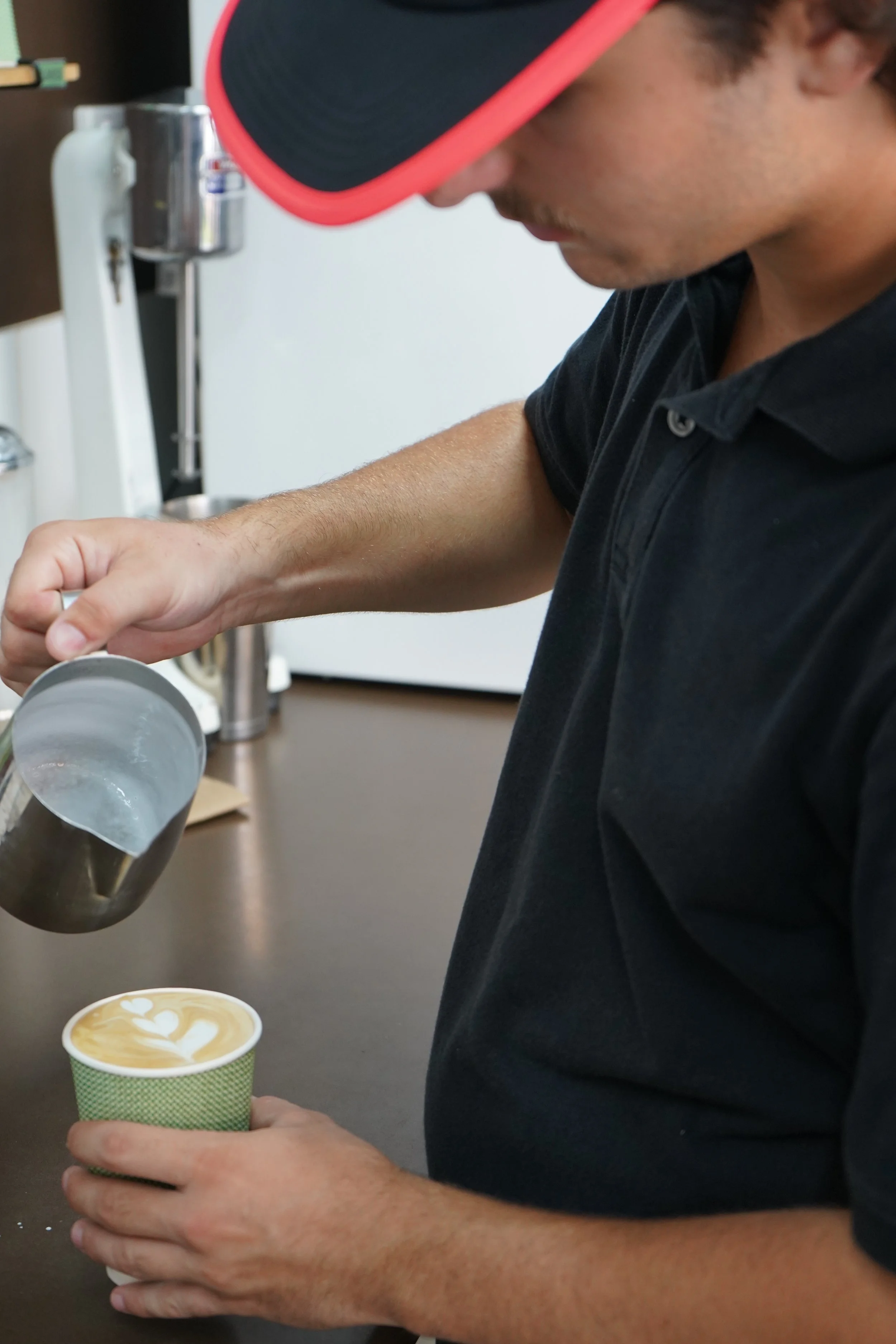 Man pouring steamed milk into a cup of coffee with latte art.