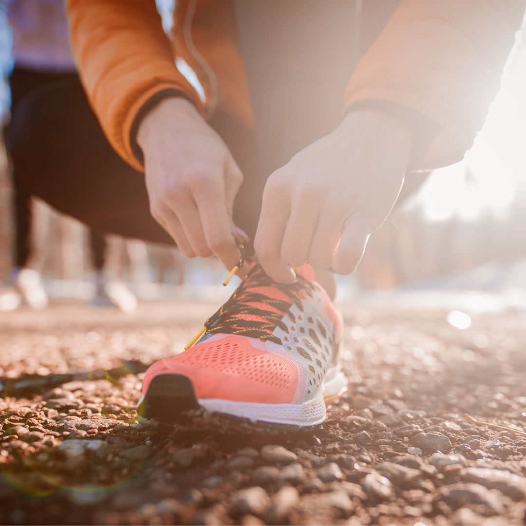 Person tying running shoes outdoors on gravel path in sunlight.