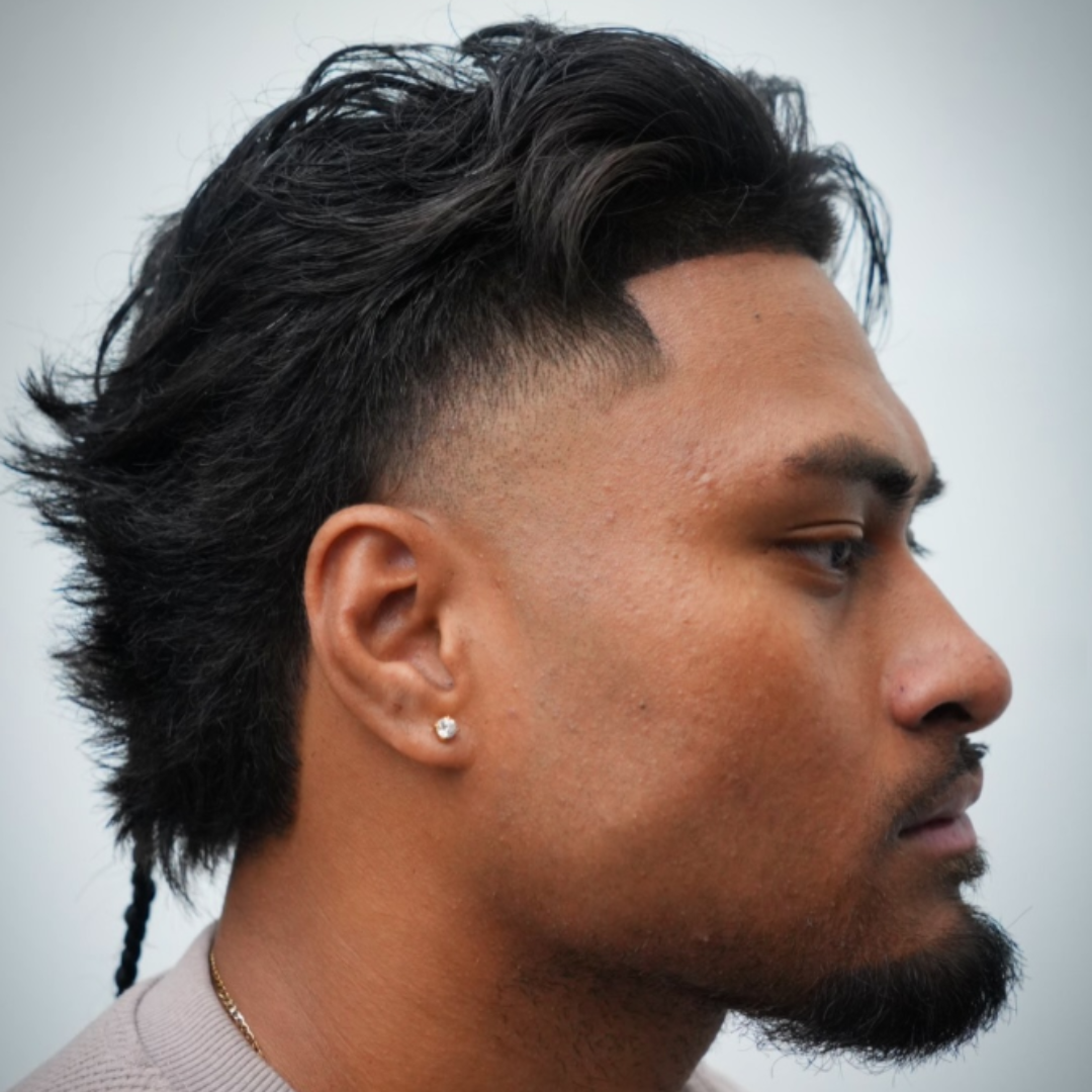Side profile of a man with a stylish haircut, earrings, and a beard.
