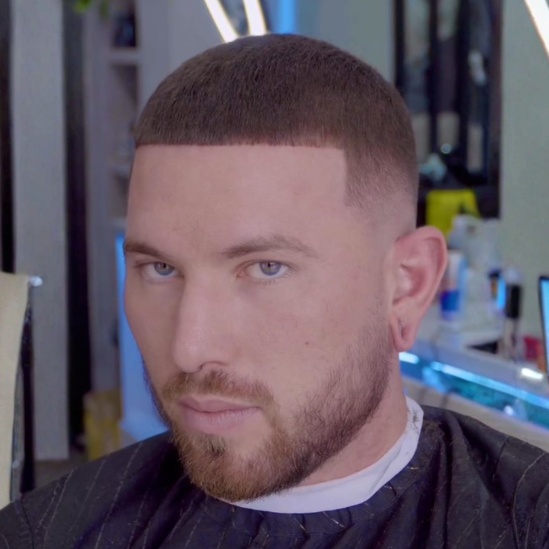 Man with a fresh haircut, beard, and blue eyes sitting in a barbershop.