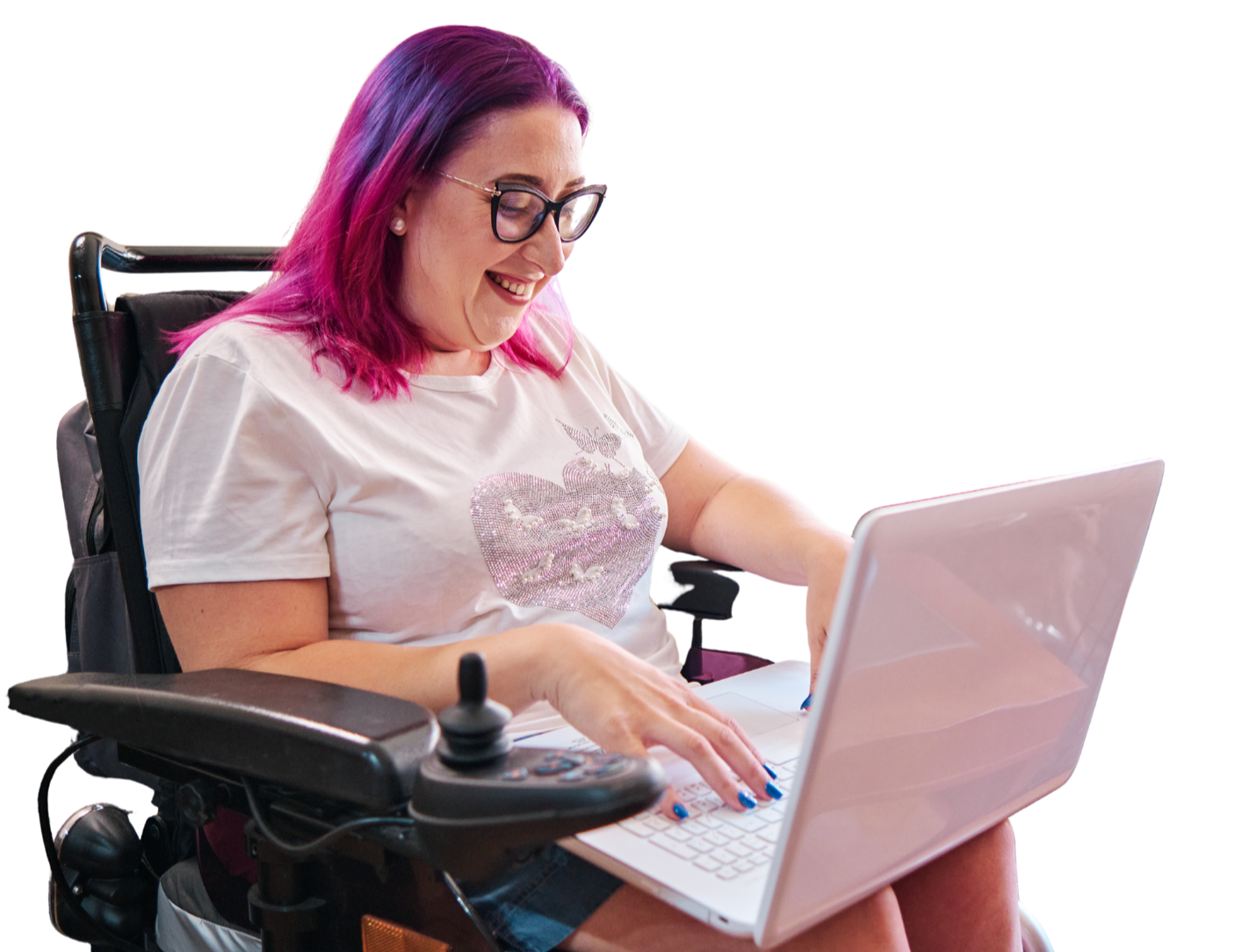 A woman with pink and purple hair, wearing glasses and a white t-shirt with a heart design, sitting in a motorized wheelchair, smiling and using a laptop.