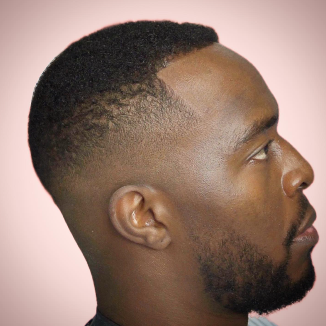 Profile of a man with a short fade haircut and beard, facing right with a light pink background.