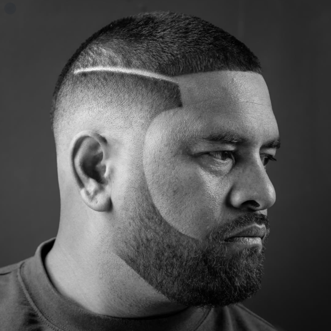 Black and white photo of a man with a close-cropped hairstyle, beard, and a tattooed beard area, looking to the right.