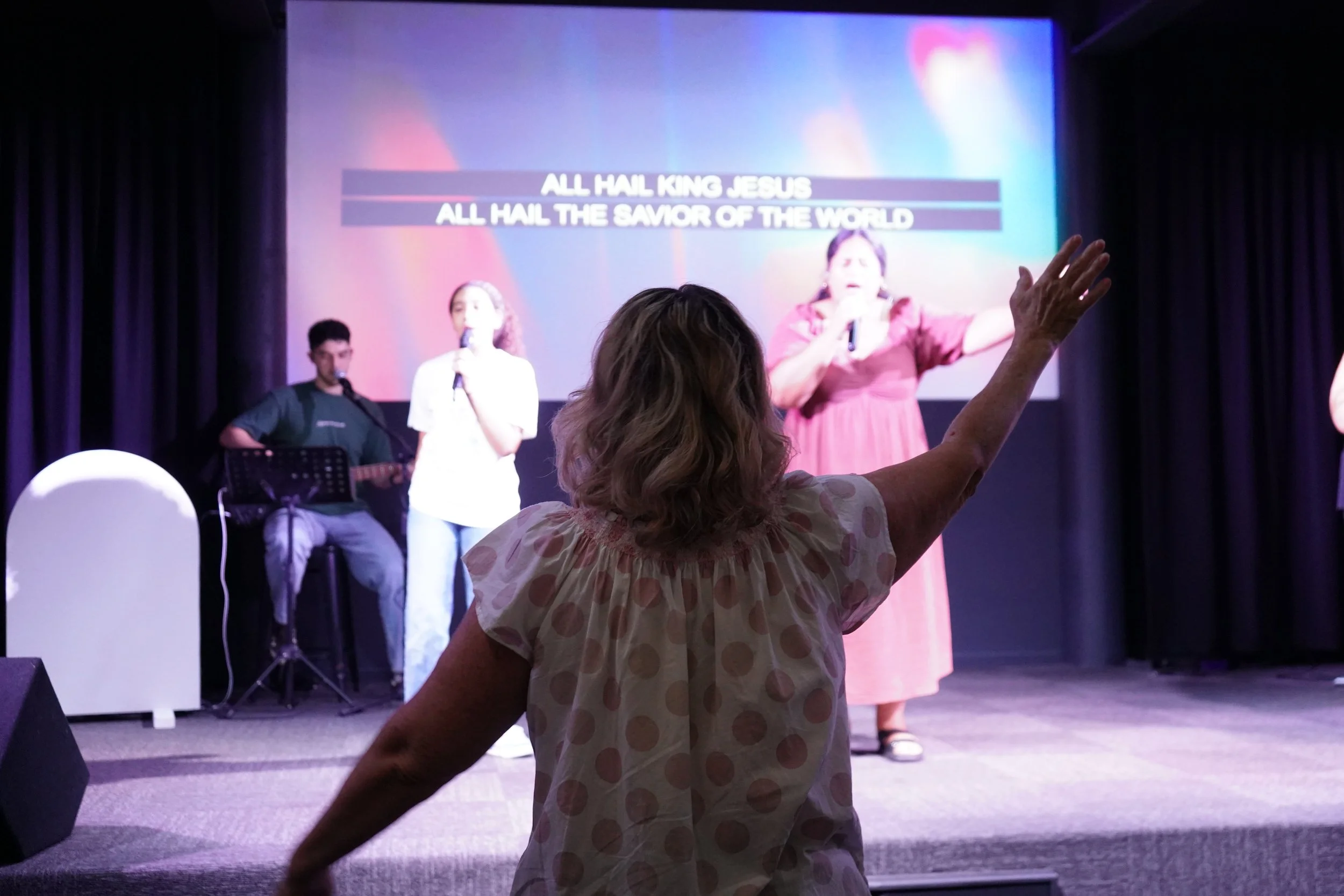 A woman worshiping in the front row at Twin Rivers Church as the worship team leads the congregation in praise.