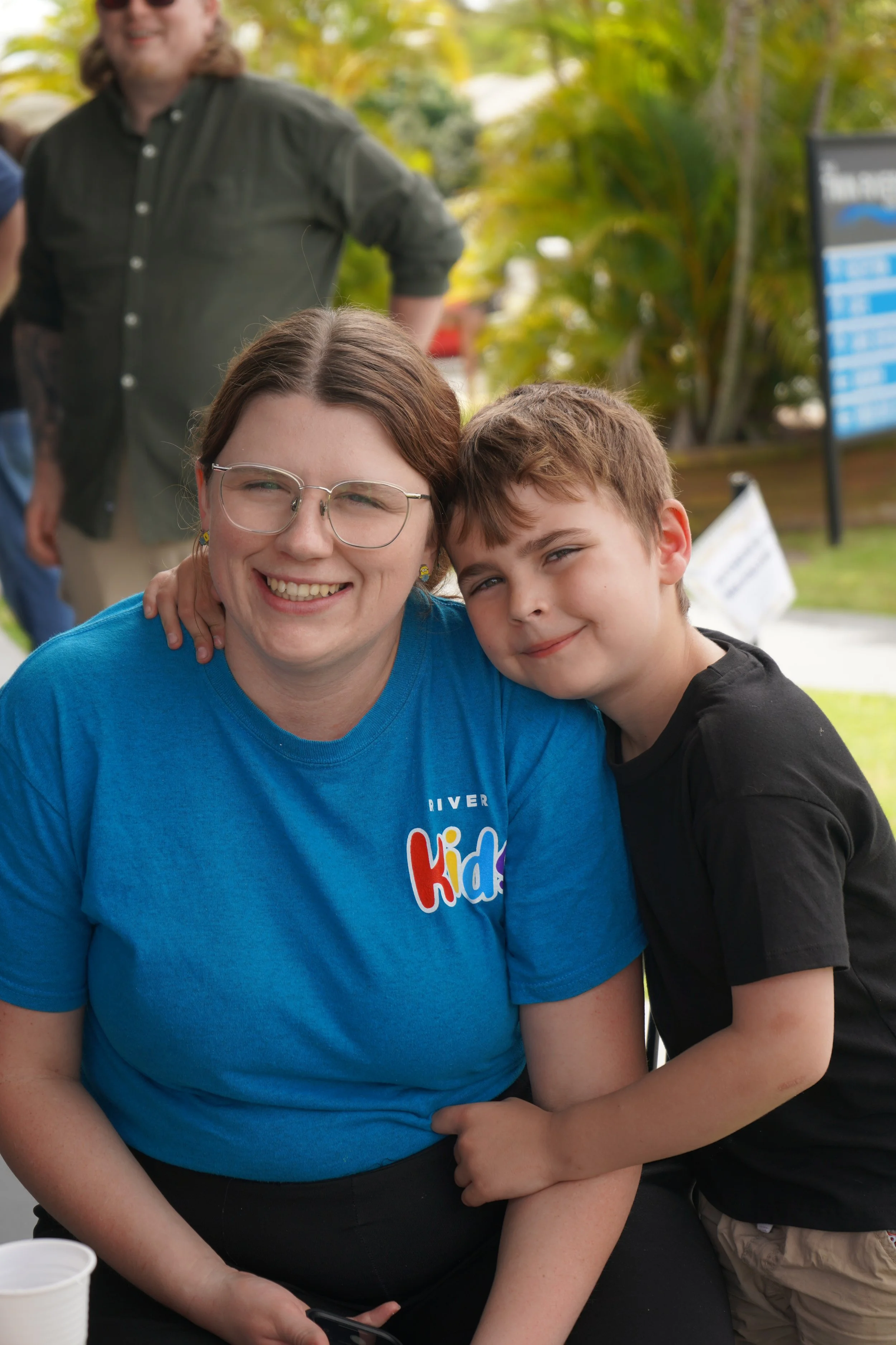 Our friendly river kids leader, Maddie smiling with her son wearing the blue river kids t-shirt.