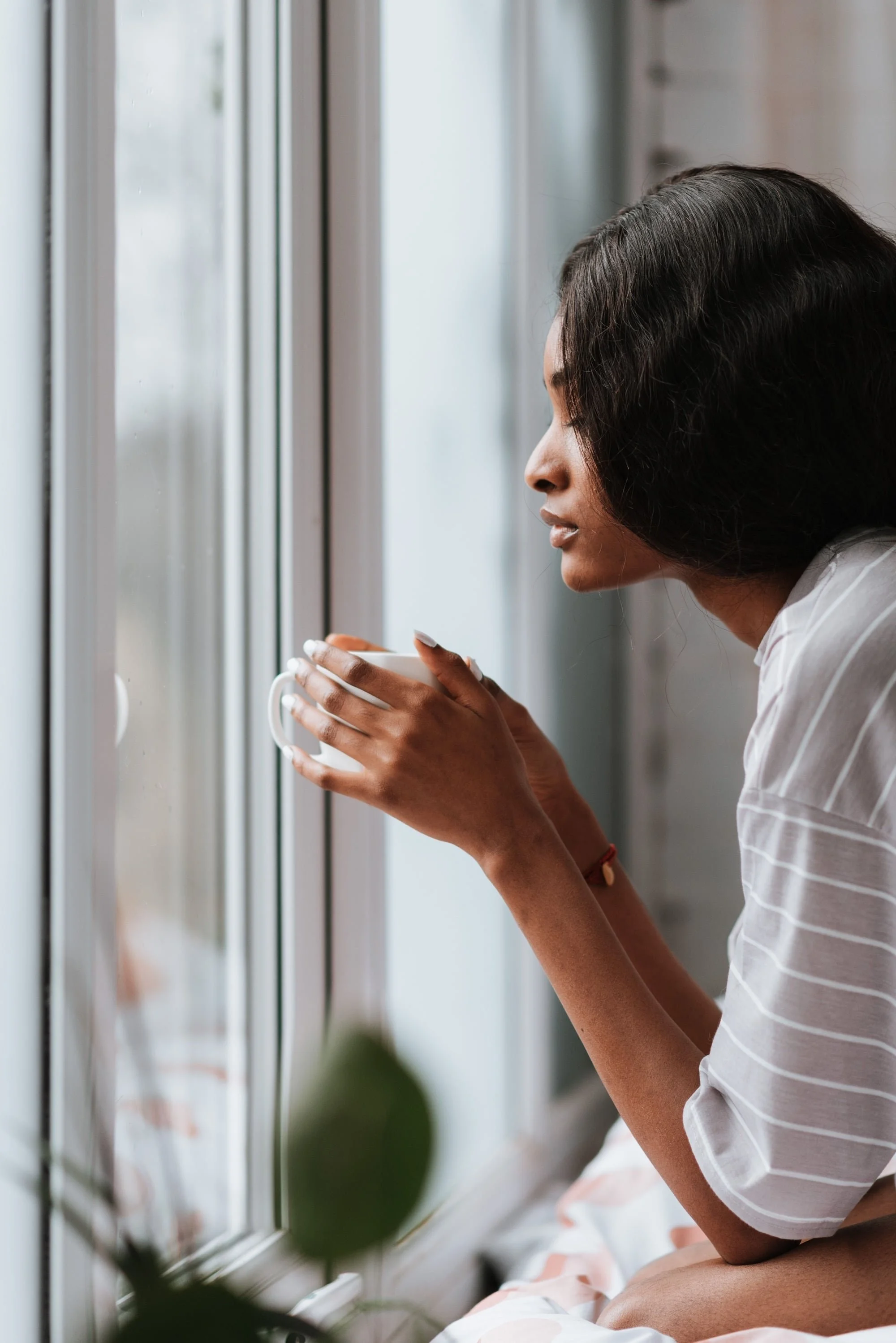 Woman gazing out a window while holding a warm cup of coffee, a quiet moment of reflection.