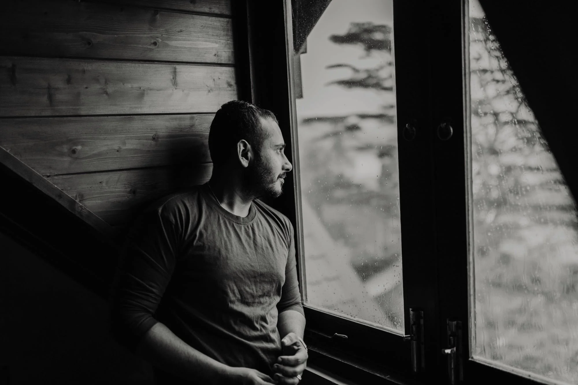 Hispanic man looking outside of a window during a rainy day.