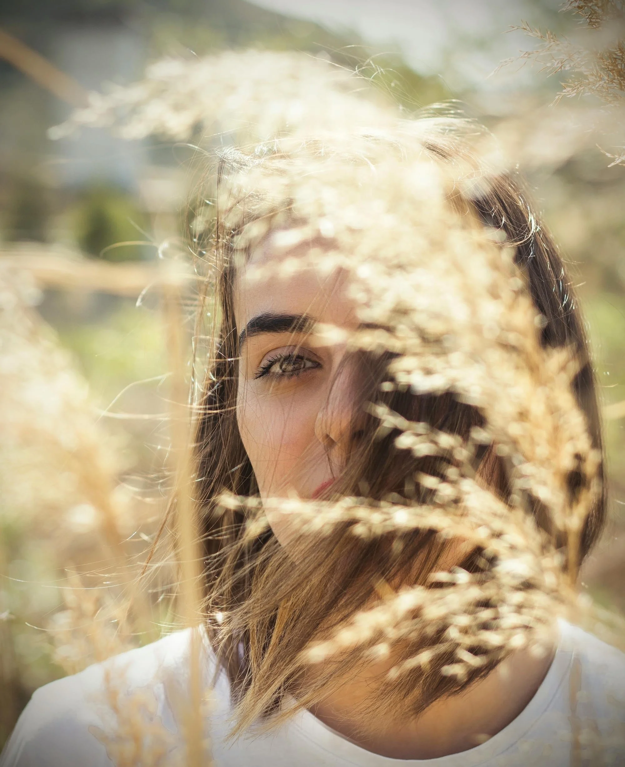 Woman with brown hair partially obscured by golden wild grass in a sunlit field, representing the feeling of being stuck in the past