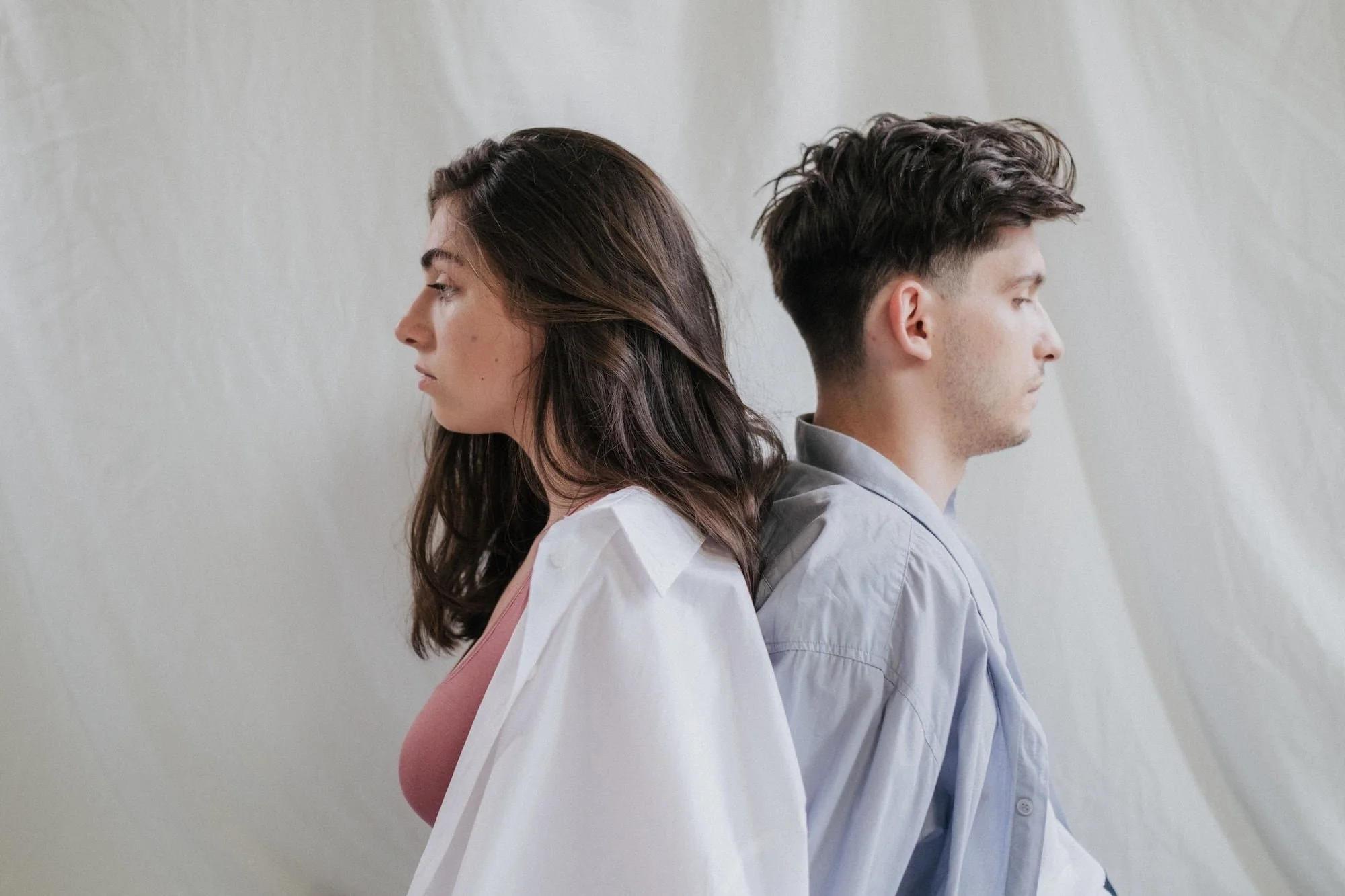 Two young adults standing back to back looking away from each other, reflecting the isolation and relationship challenges that bring many people to young adult therapy