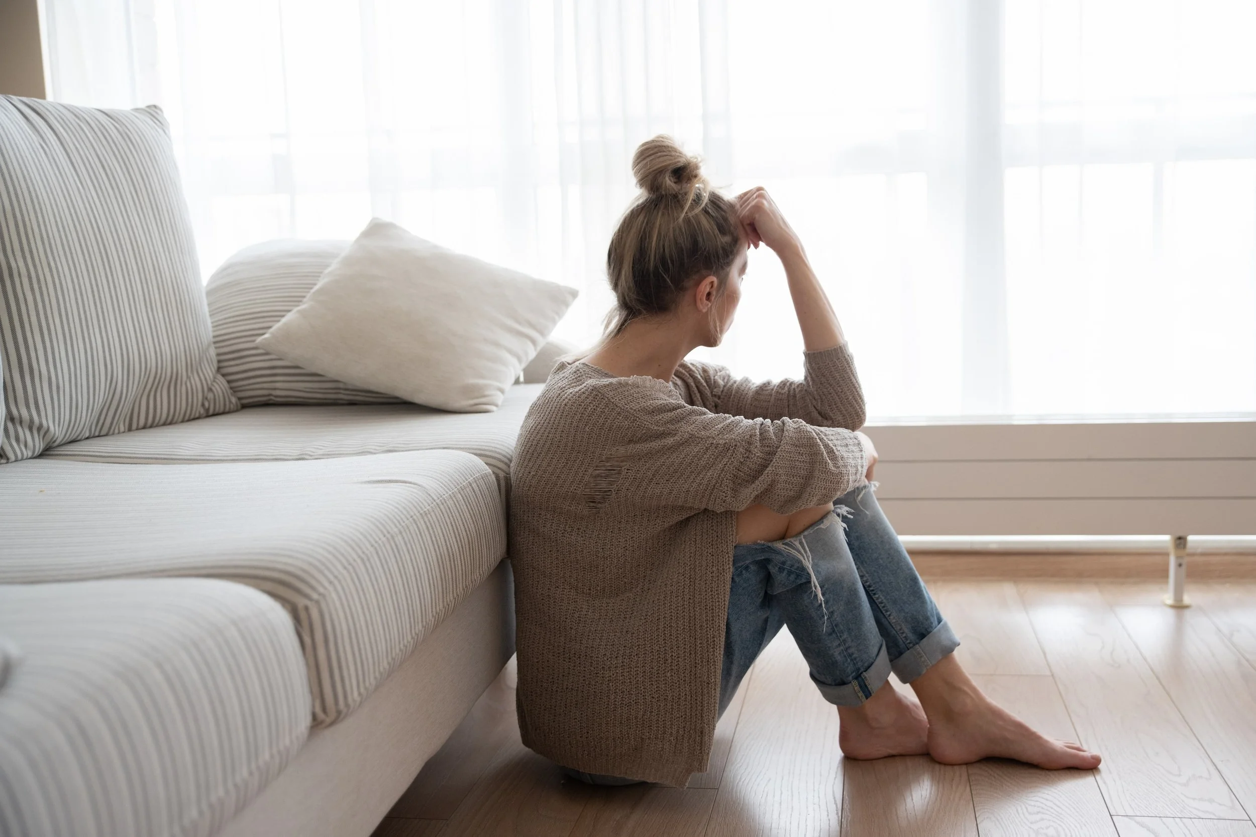 Woman experiencing anxiety or depression sitting alone by window, representing the emotional struggles addressed in therapy