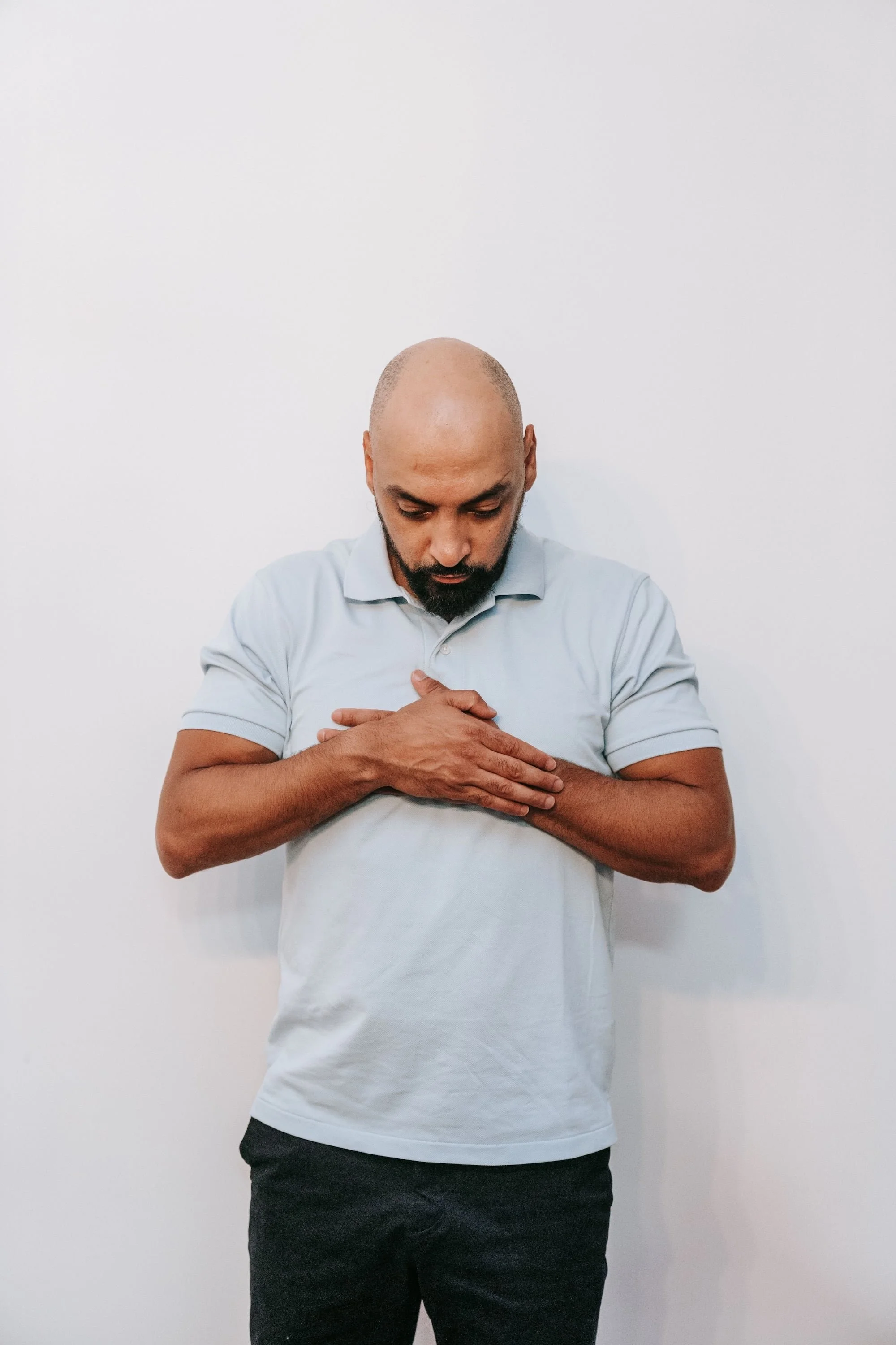 Man standing with eyes closed, both hands resting over his heart in a calming gesture.
