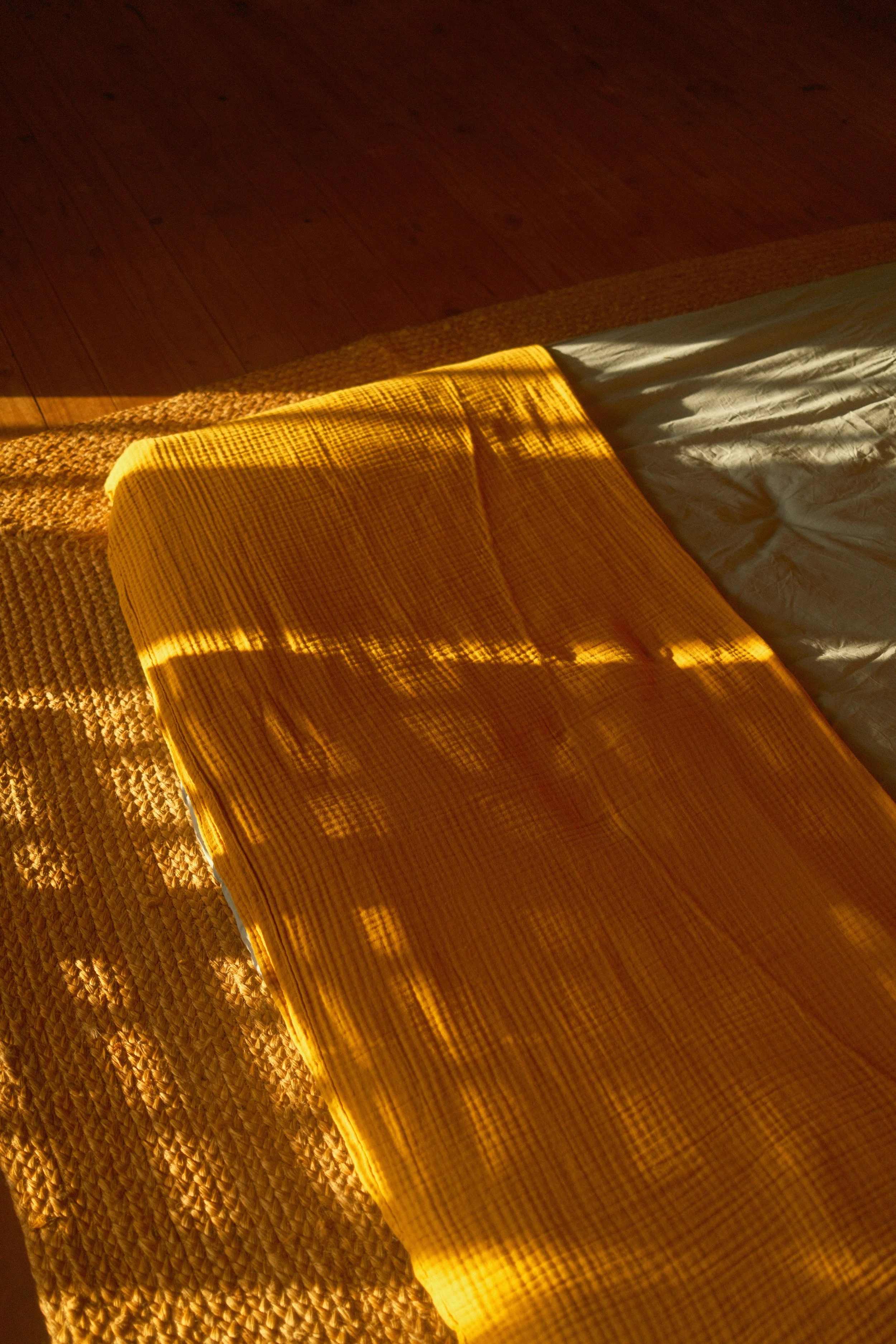 Un lit avec une couverture jaune et un lit à côté, la lumière du soleil illumine la couverture et le sol en bois en arrière-plan.