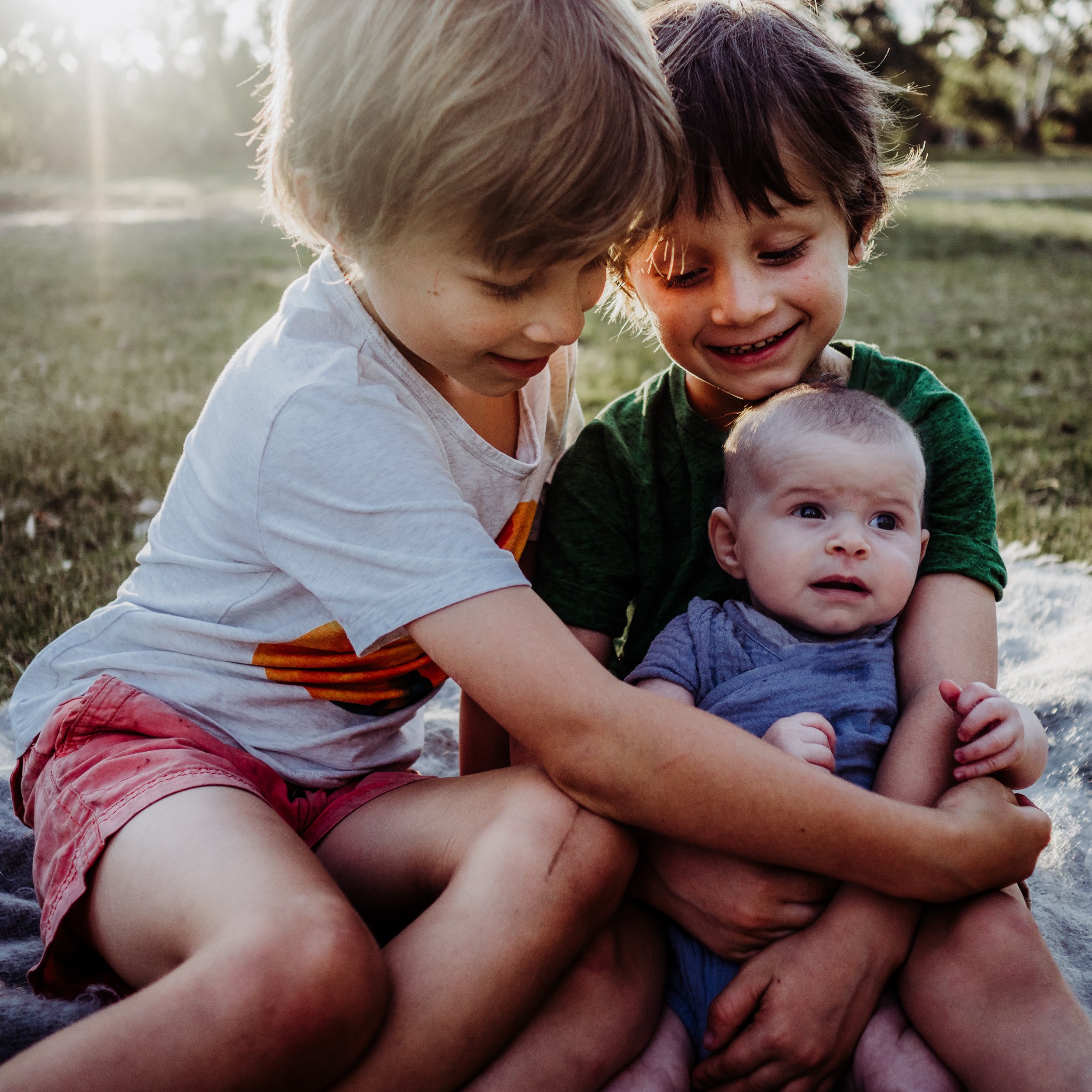 Two big brothers cuddle there baby sister. The sun sets behind them