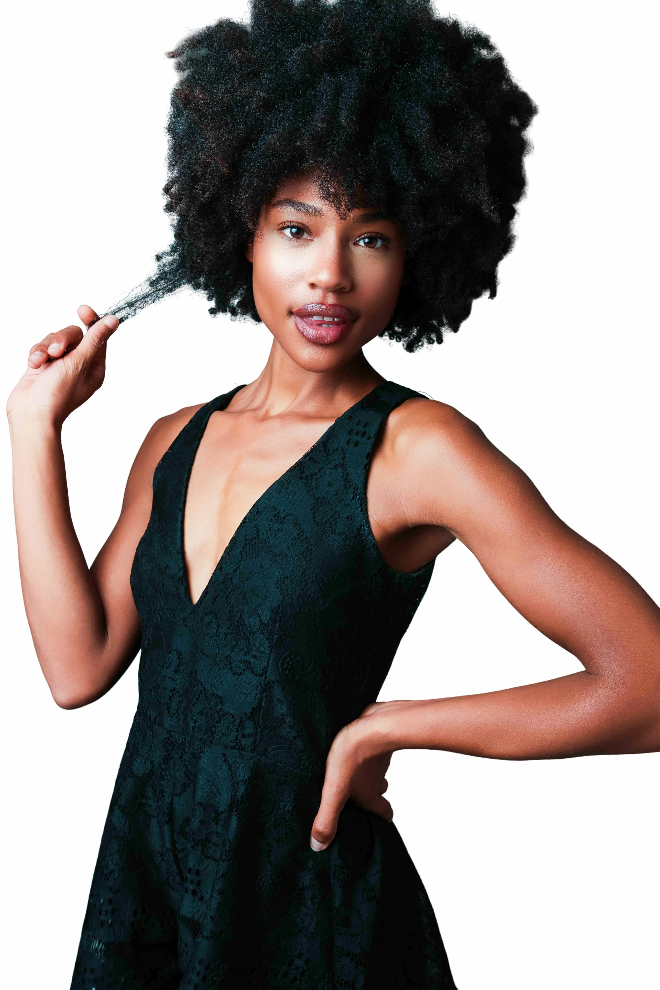 A woman with natural curly hair wearing a black sleeveless dress, posing against a white background.