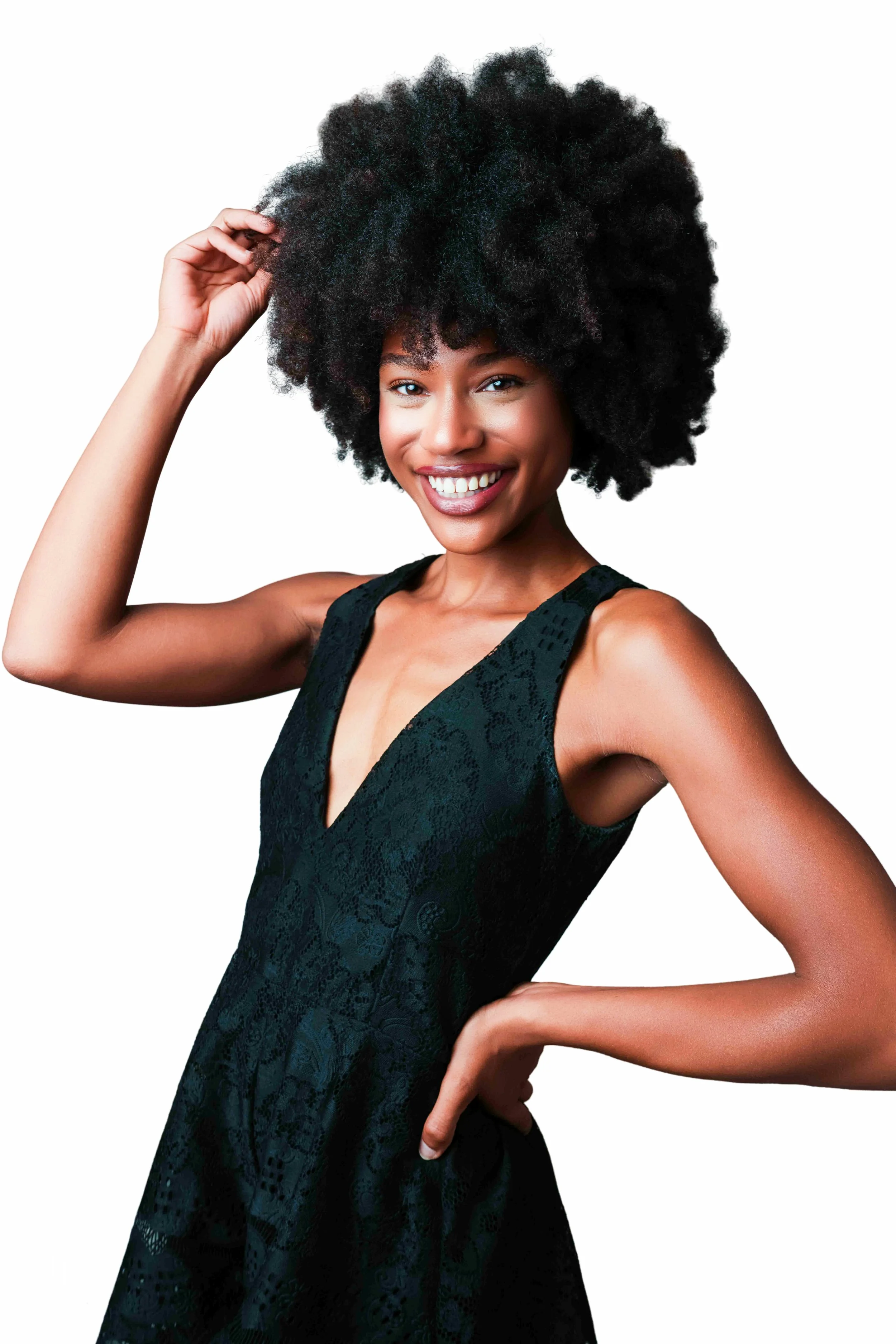 A woman with dark skin and a large, curly afro hairstyle, smiling and wearing a black patterned sleeveless dress, against a plain white background.