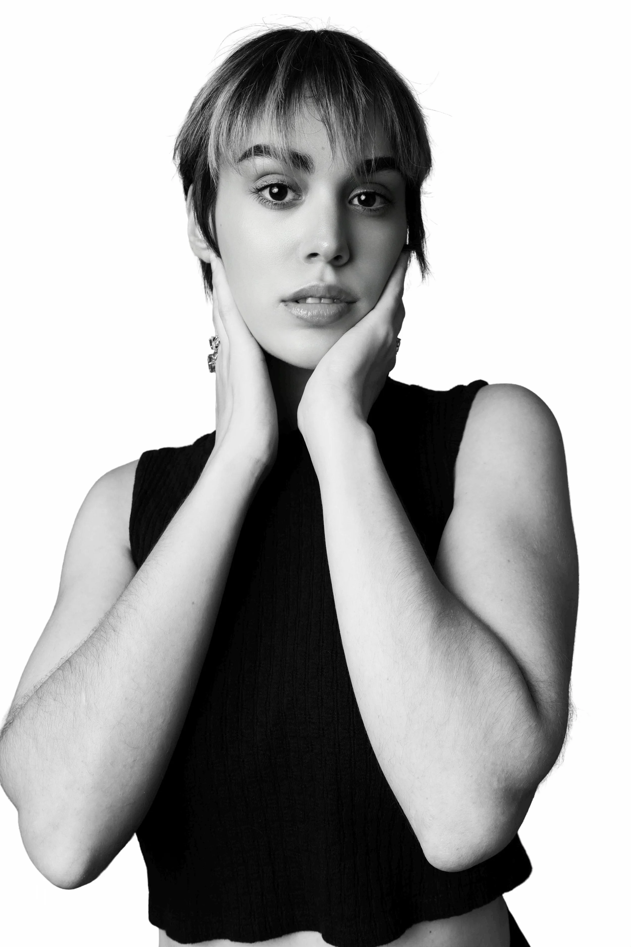 Black and white portrait of a woman with short, layered hair, wearing a sleeveless top, with her hands gently touching her face.