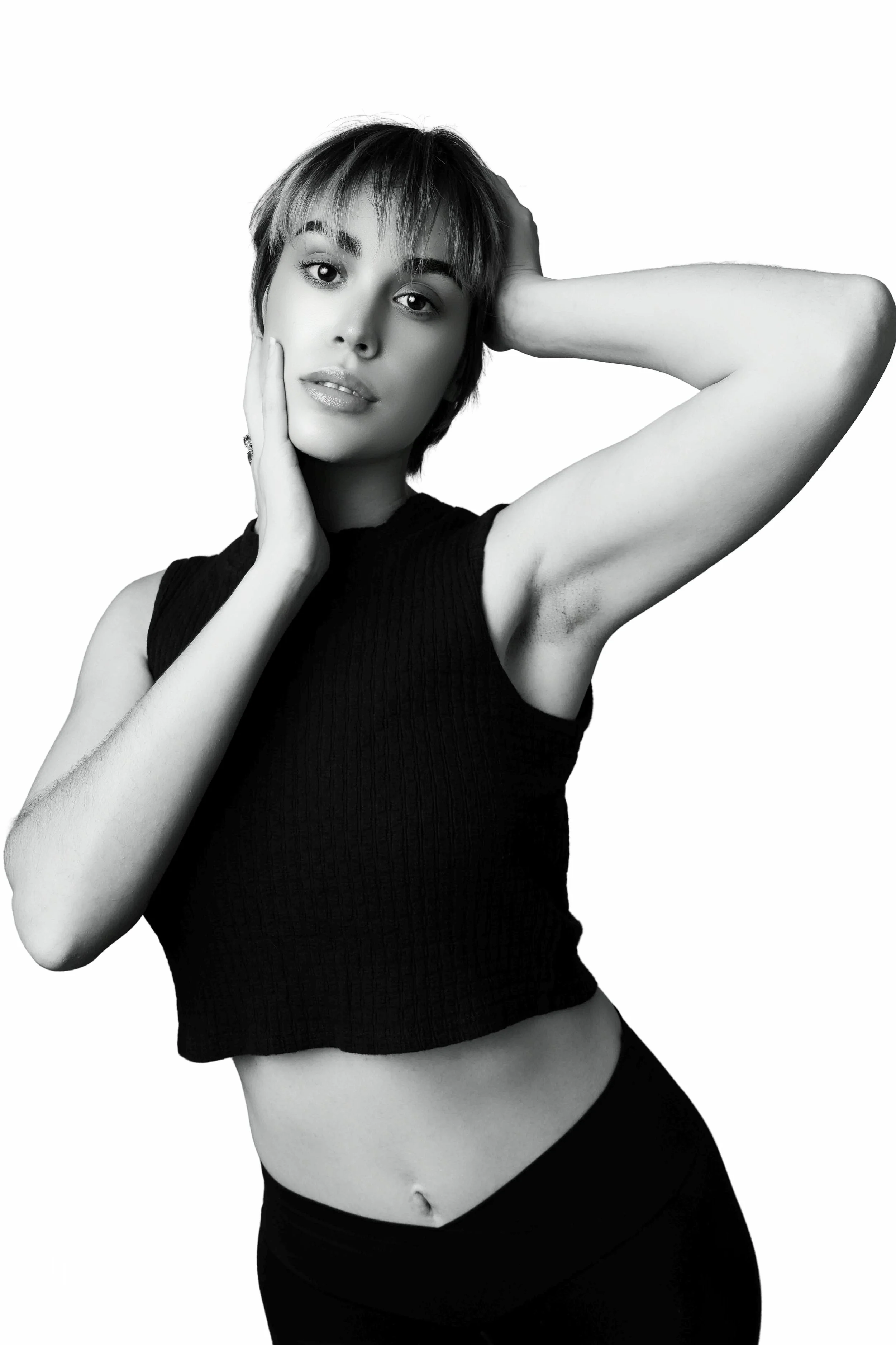 Black and white portrait of a young woman with short hair, wearing a sleeveless top and leggings, posing with one hand on her face and the other behind her head.