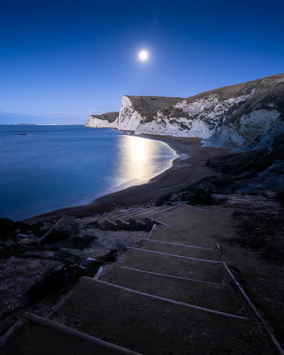 Full moon setting over bats head in dorset durdle door during winter at blue hour with the staircase in the foreground