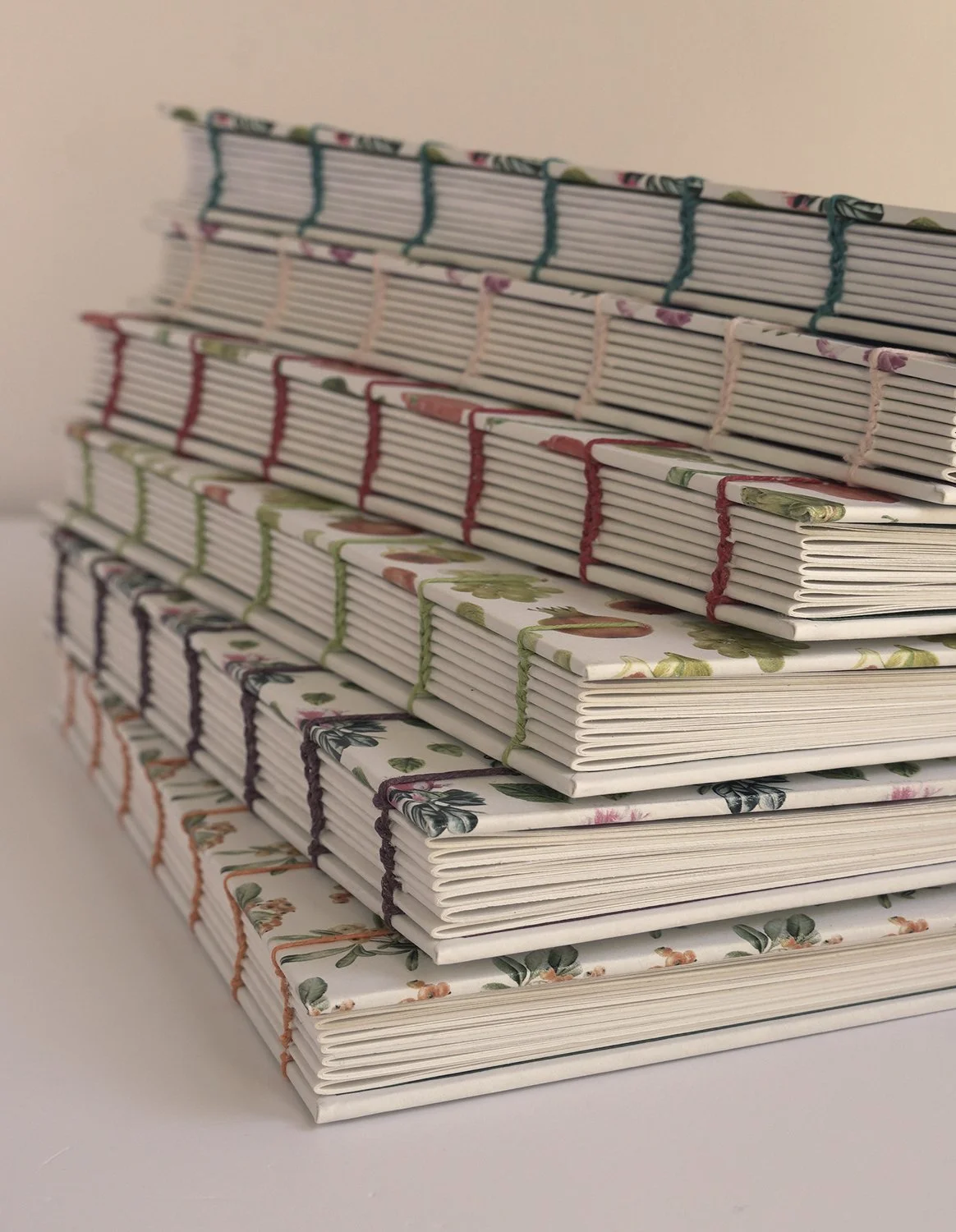 Cuadernos apilados encuadernados artesanalmente con hilos de lino encerados de diferentes colores.