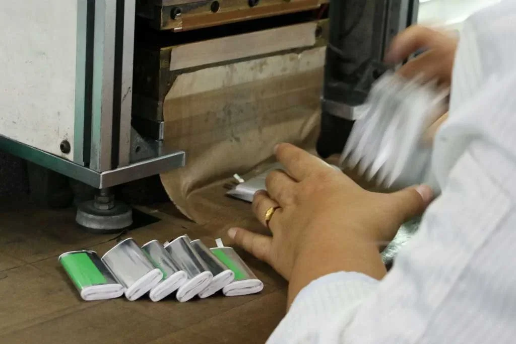 Person using a machine to produce metallic objects, with several finished metallic items in front, likely aluminum cans or similar items.