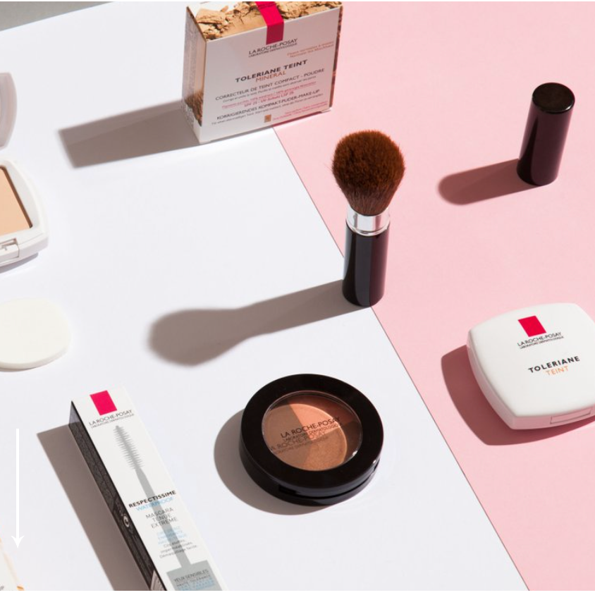 Make-up-Produkte, darunter Puder, Blush, Lippenstift und Pinsel, auf einer weißen und pinken Oberfläche