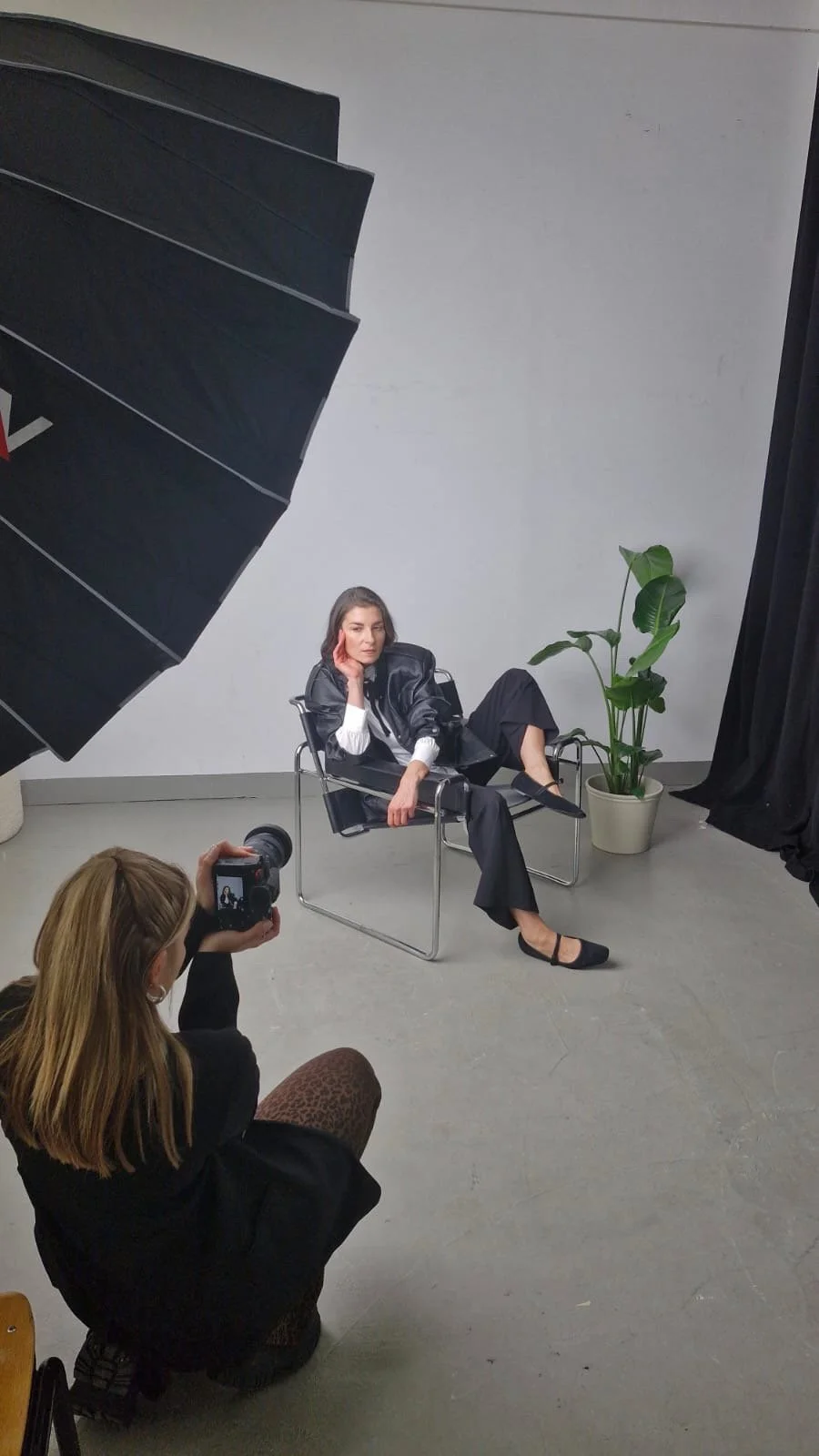 Frau posiert bei Fotoshooting in Studio, sitzt auf Stuhl, während Fotografin im Vordergrund fotografiert.