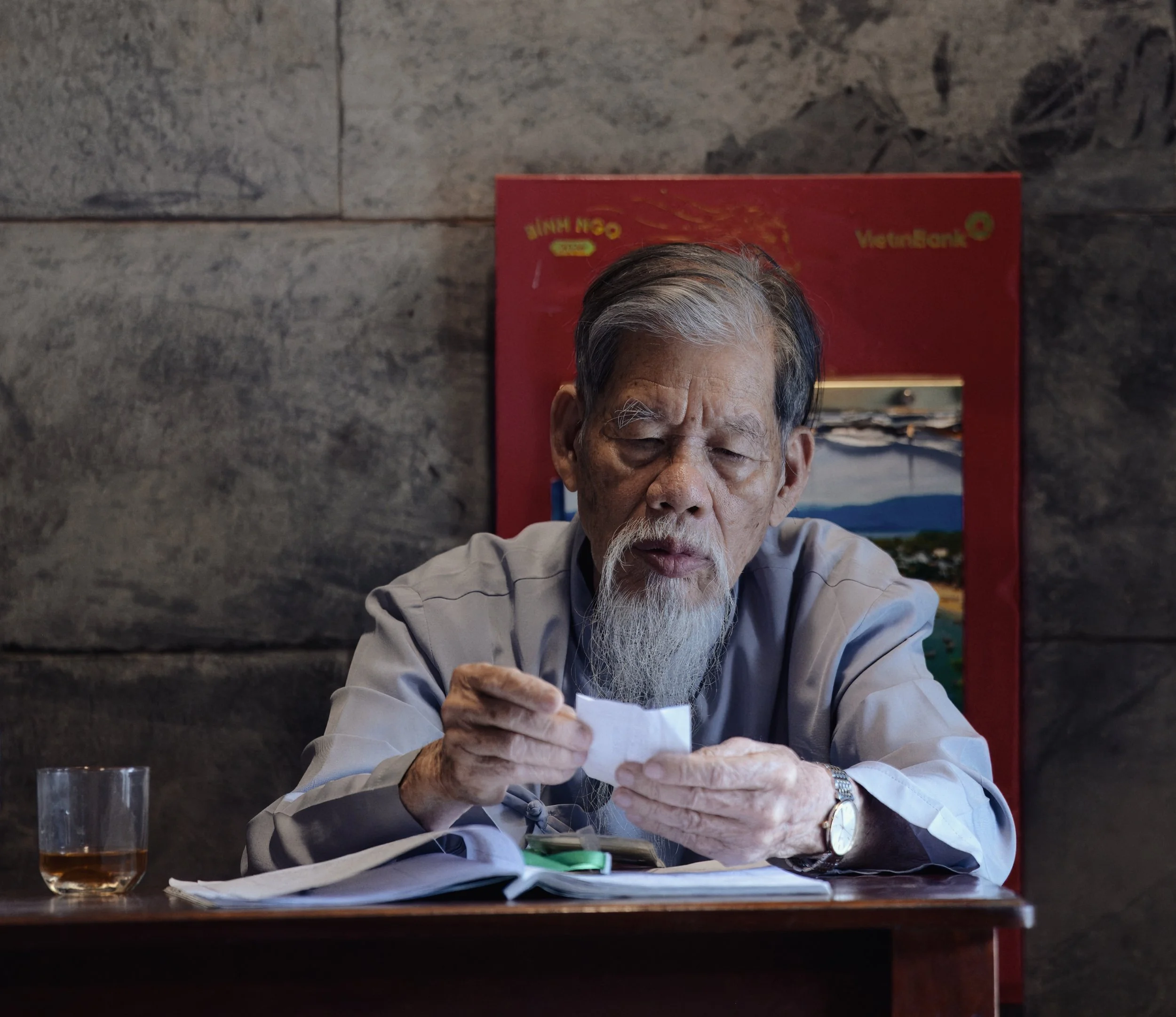 Portrait of an older man reading a small note at a table in Hanoi