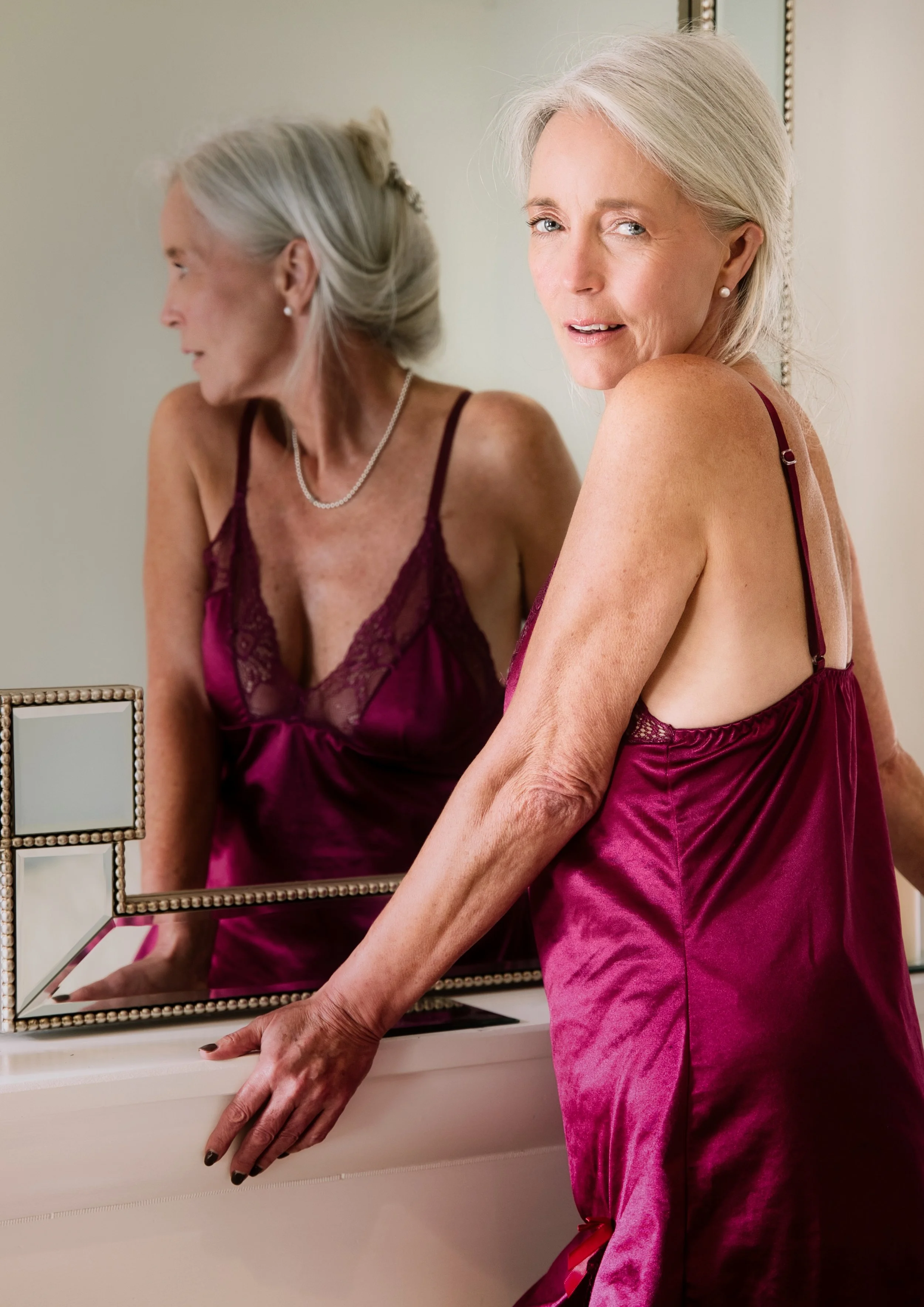 Portrait of a woman beside a mirror wearing satin lingerie
