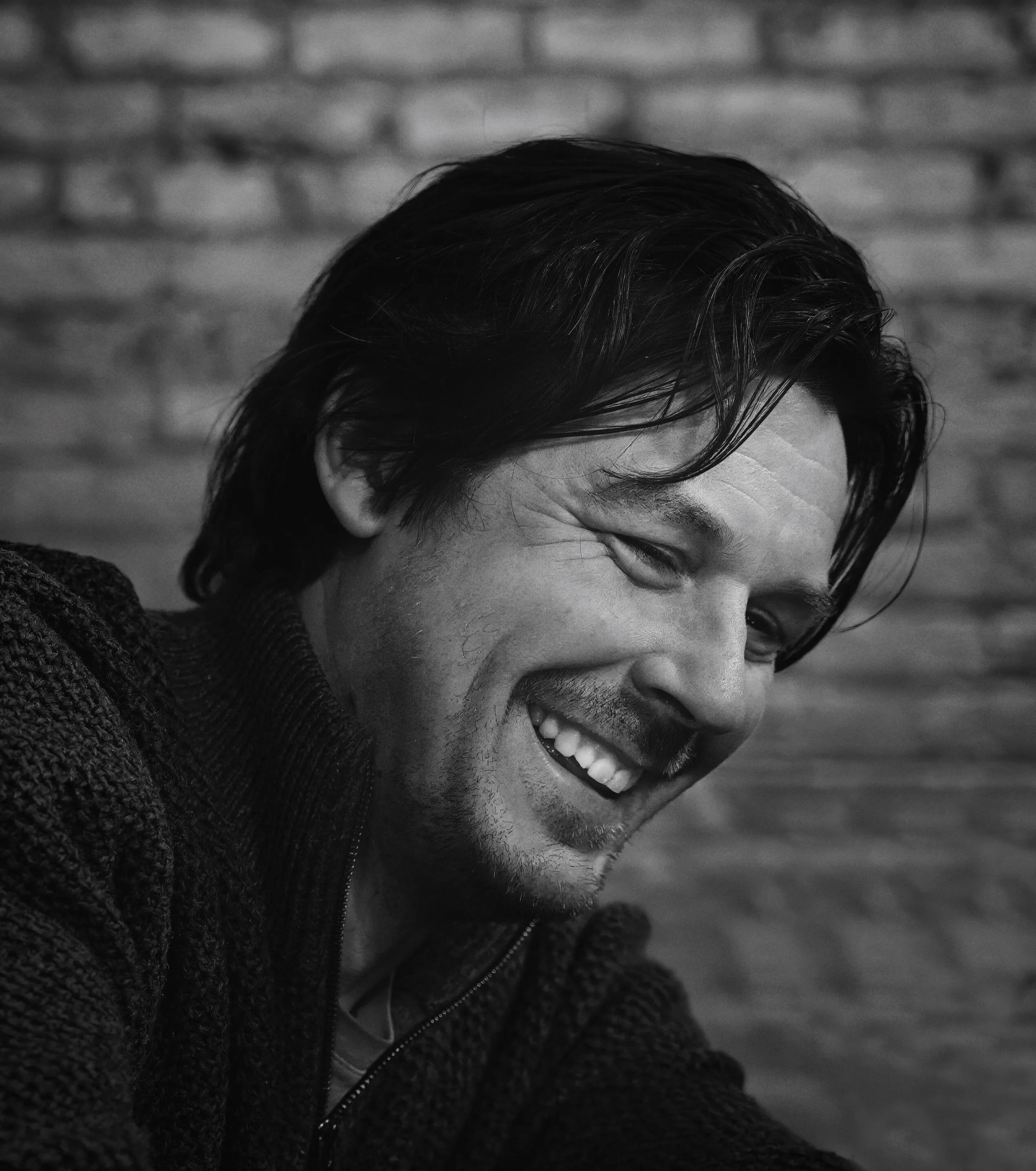 Black and white portrait of a smiling man against a brick wall