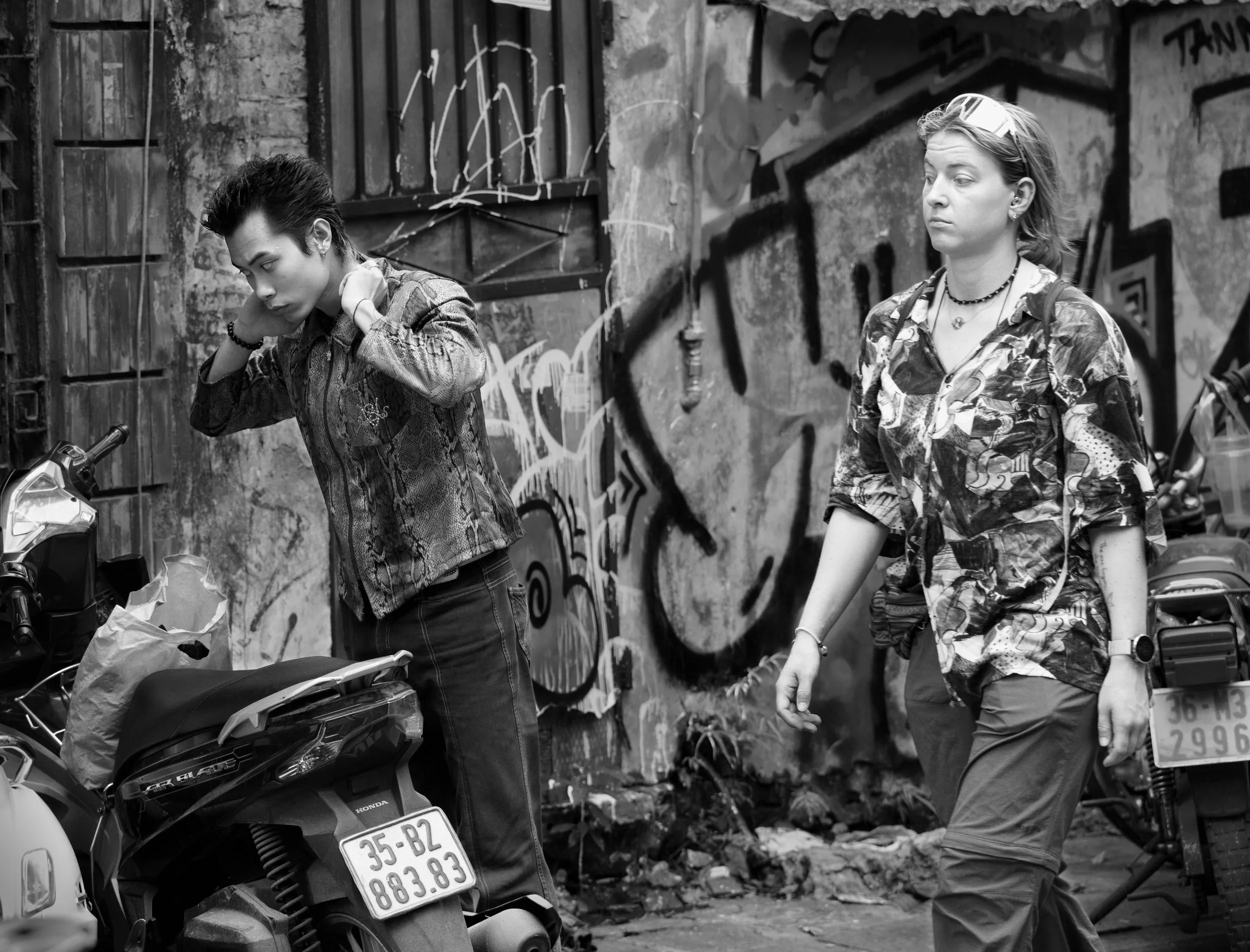 Black and white street photograph of two people passing each other beside graffiti-covered walls in Hanoi