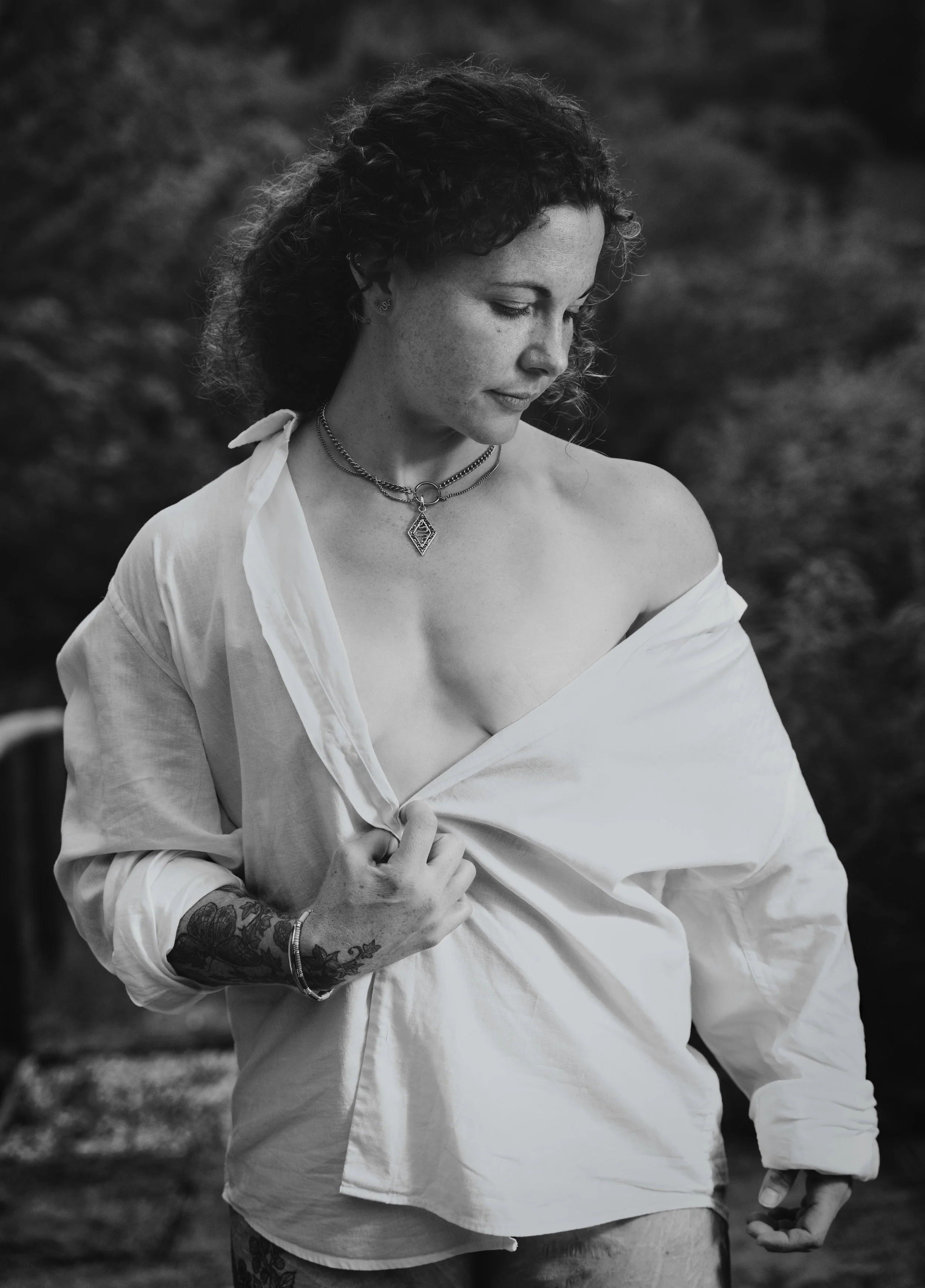 Black and white portrait of a woman wearing an oversized white shirt outdoors, photographed in soft natural light.