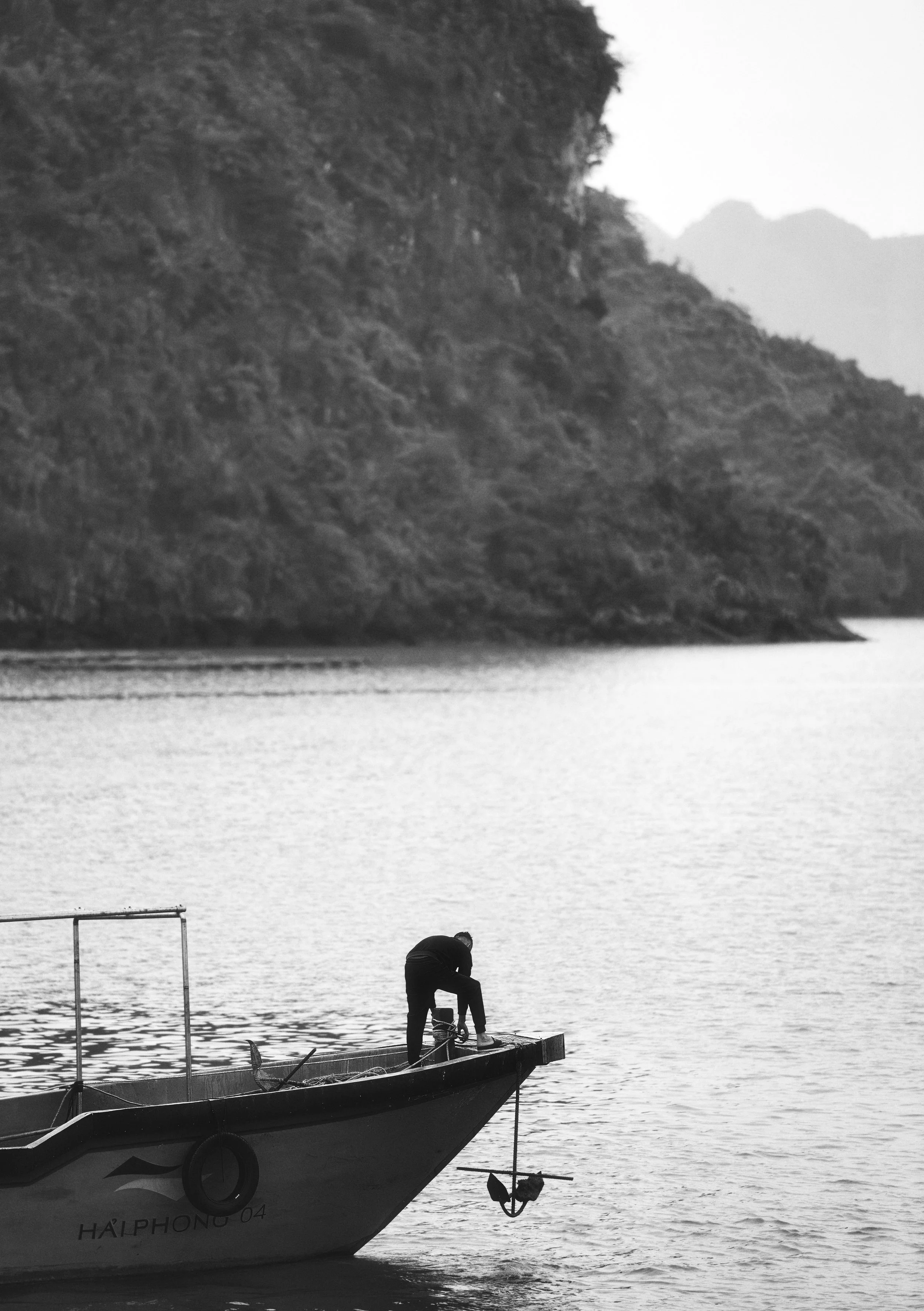 Black and white photograph of a lone figure standing on a boat in Ha Long Bay