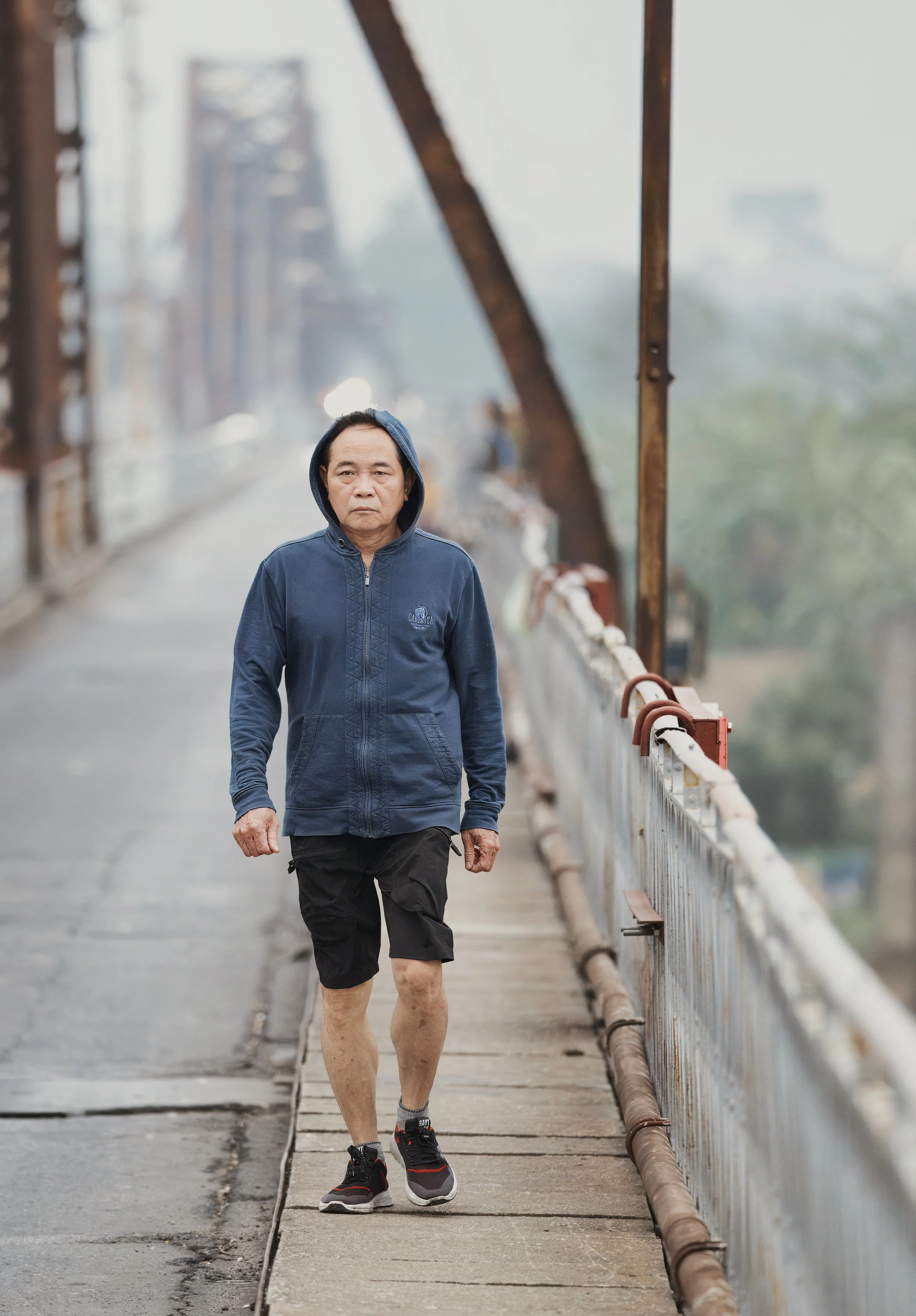 Portrait of a man walking across Long Bien Bridge in soft morning haze