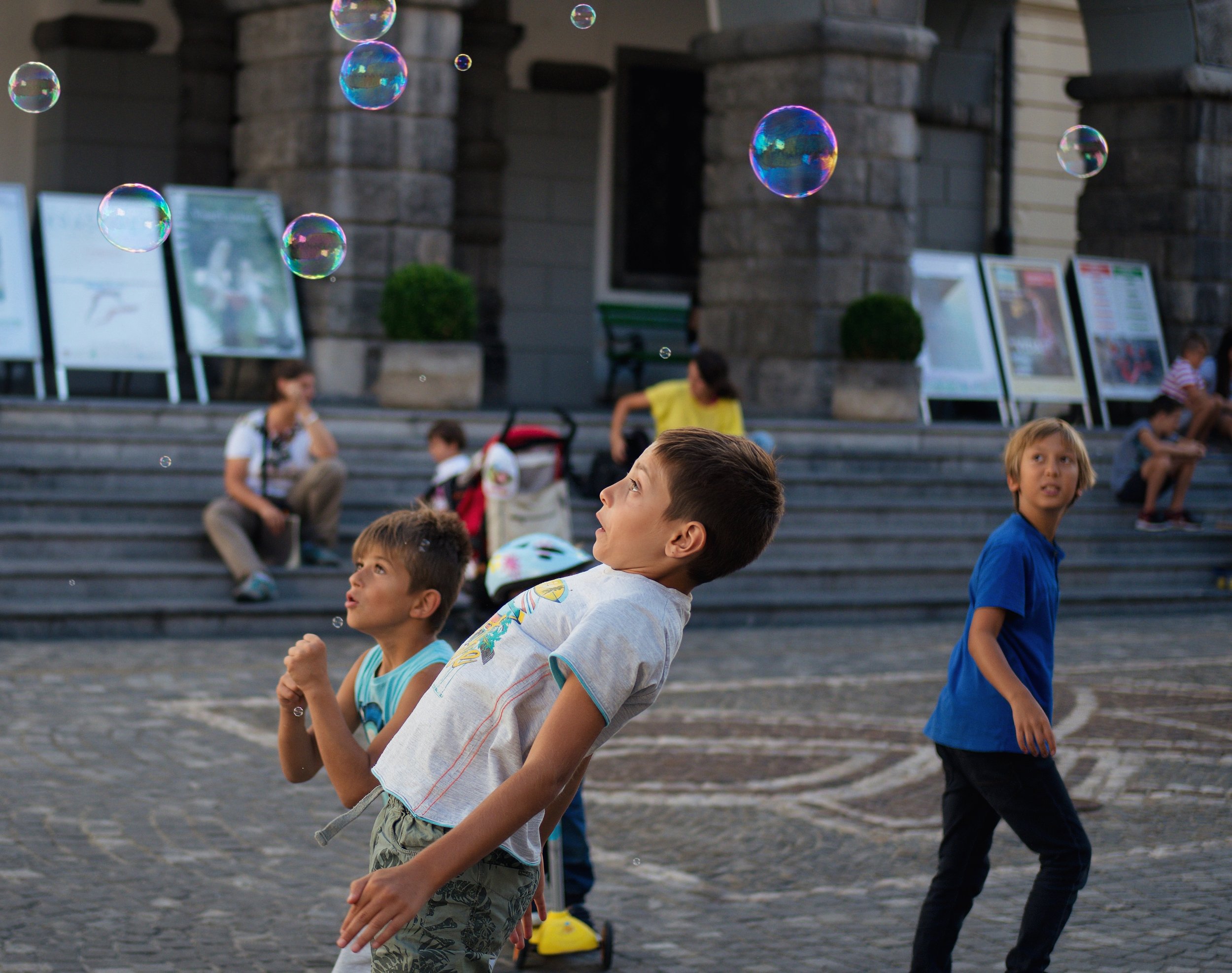 Children playing with floating bubbles in a public square in Ljubljana