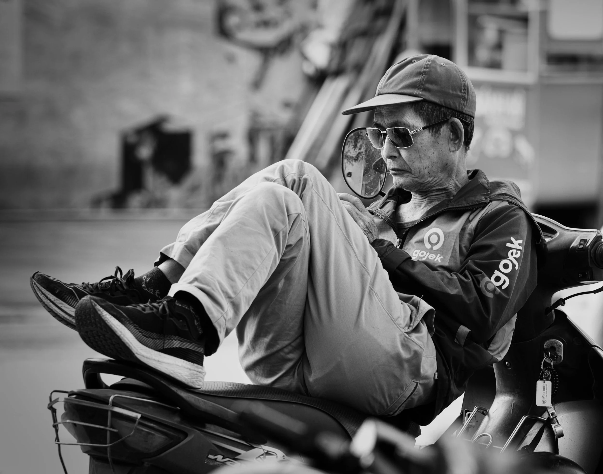 Man in sunglasses and a cap reclining on a motorbike in Hanoi, absorbed in his phone